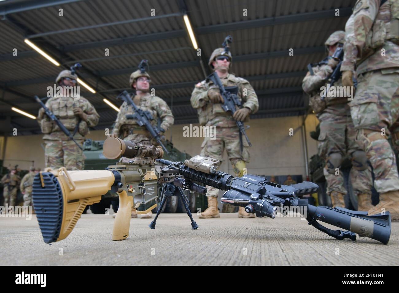 The photo displays an HK M110 Squad Designated Marksman Rifle, left, and an M4A1 carbine in front of U.S. Soldiers with Palehorse Troop, 4th Squadron, 2nd Cavalry Regiment ahead of a training exercise on Rose Barracks, Vilseck, Germany, Jan. 10, 2023. 2CR provides V Corps with a lethal and agile force capable of rapid deployment throughout the European theater in order to assure allies, deter adversaries, and when ordered, defend the NATO alliance. Stock Photo