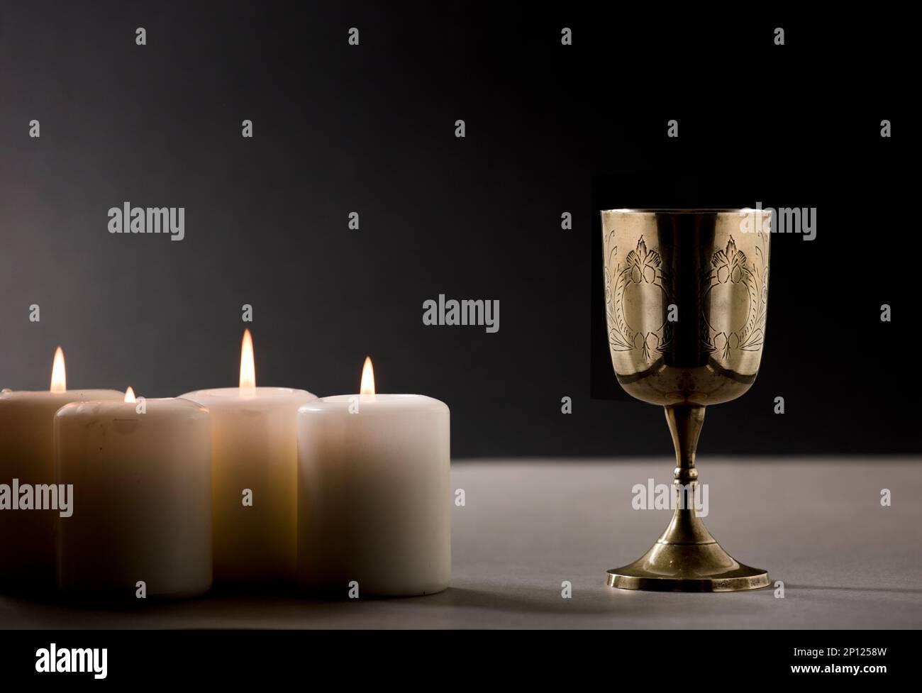 golden christian chalice with burning candles on gray altar black