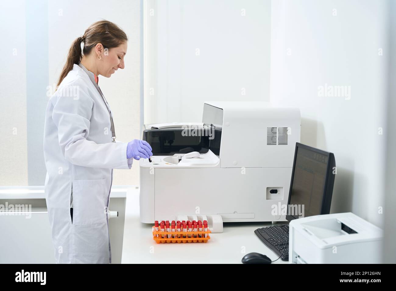 Laboratory assistant stands near a hematological analyzer in testing