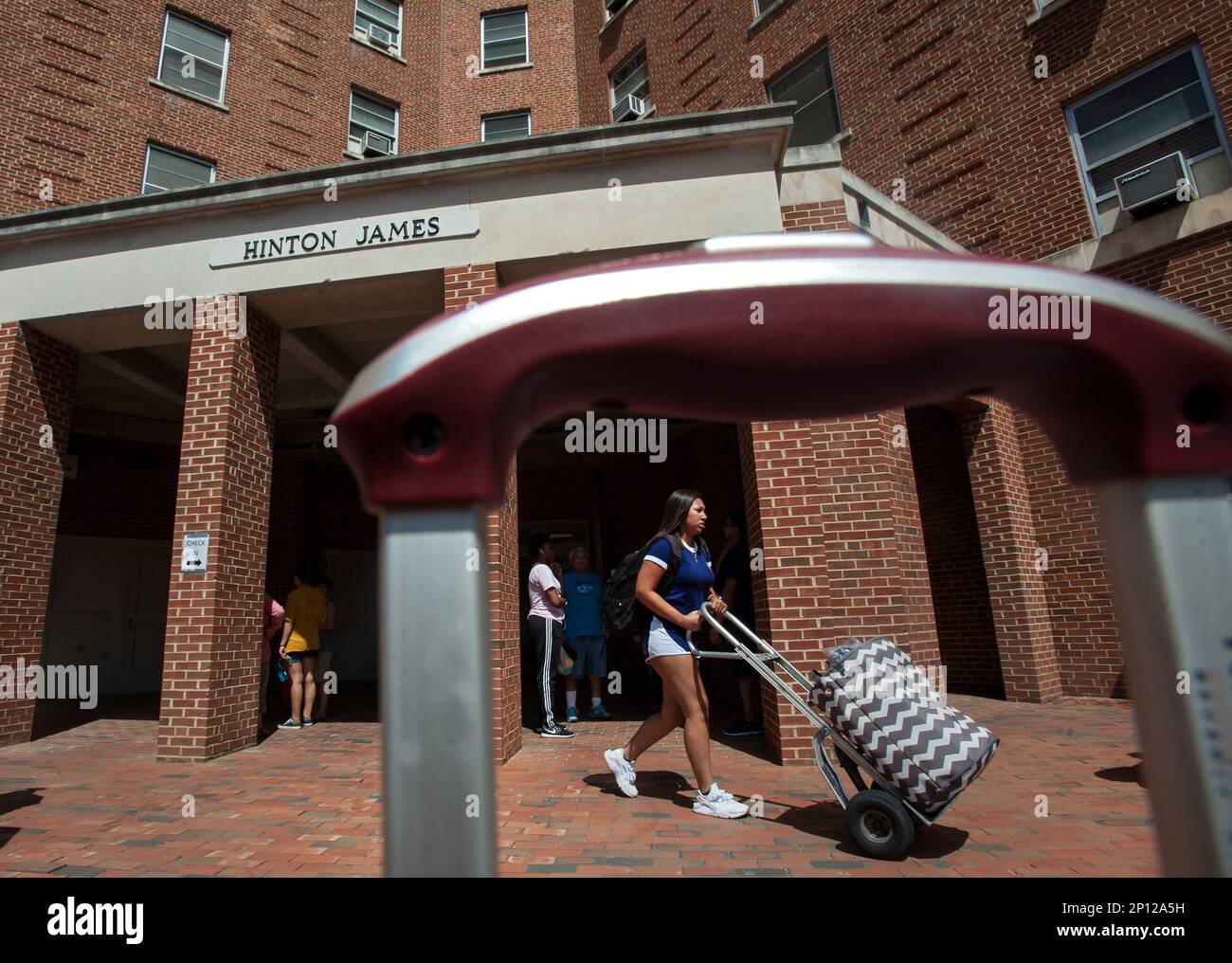 A woman rolls a suitcase in front of Hinton James Residence Hall as
