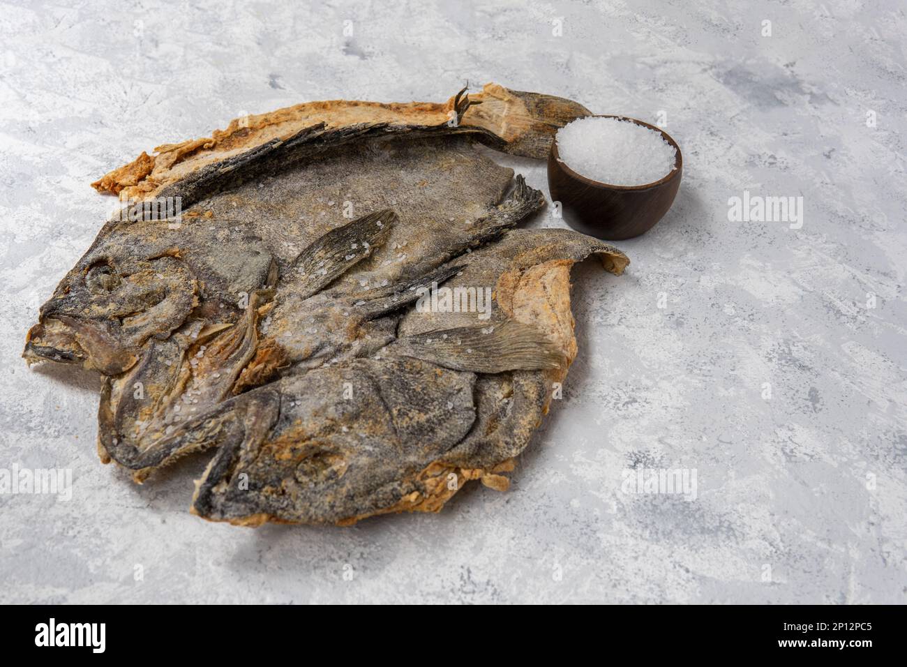Salted dry raw cod on a light textured background with a well of salt grains Stock Photo