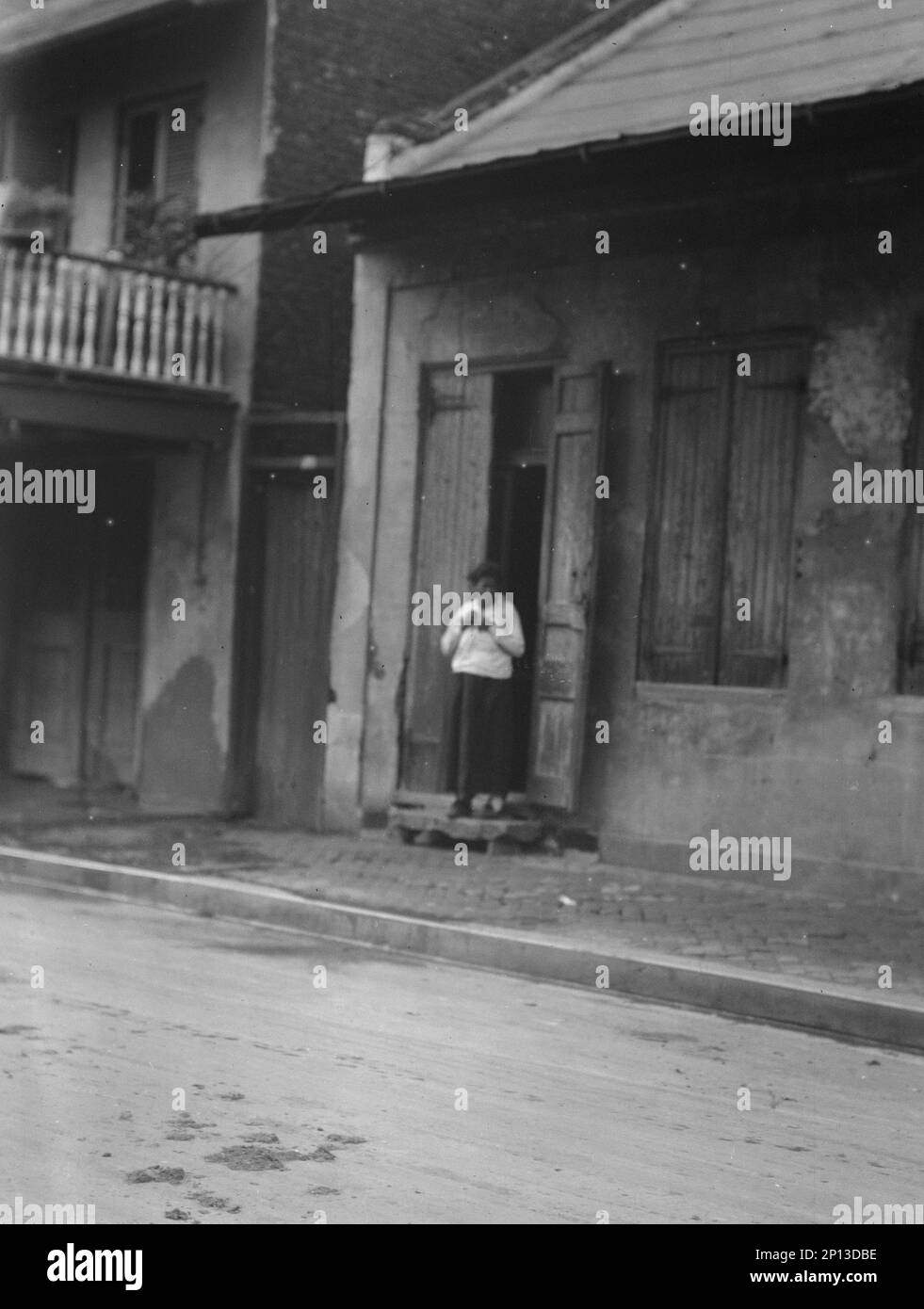 View from across street of a woman standing in a doorway in the French Quarter, New Orleans, between 1920 and 1926. Stock Photo