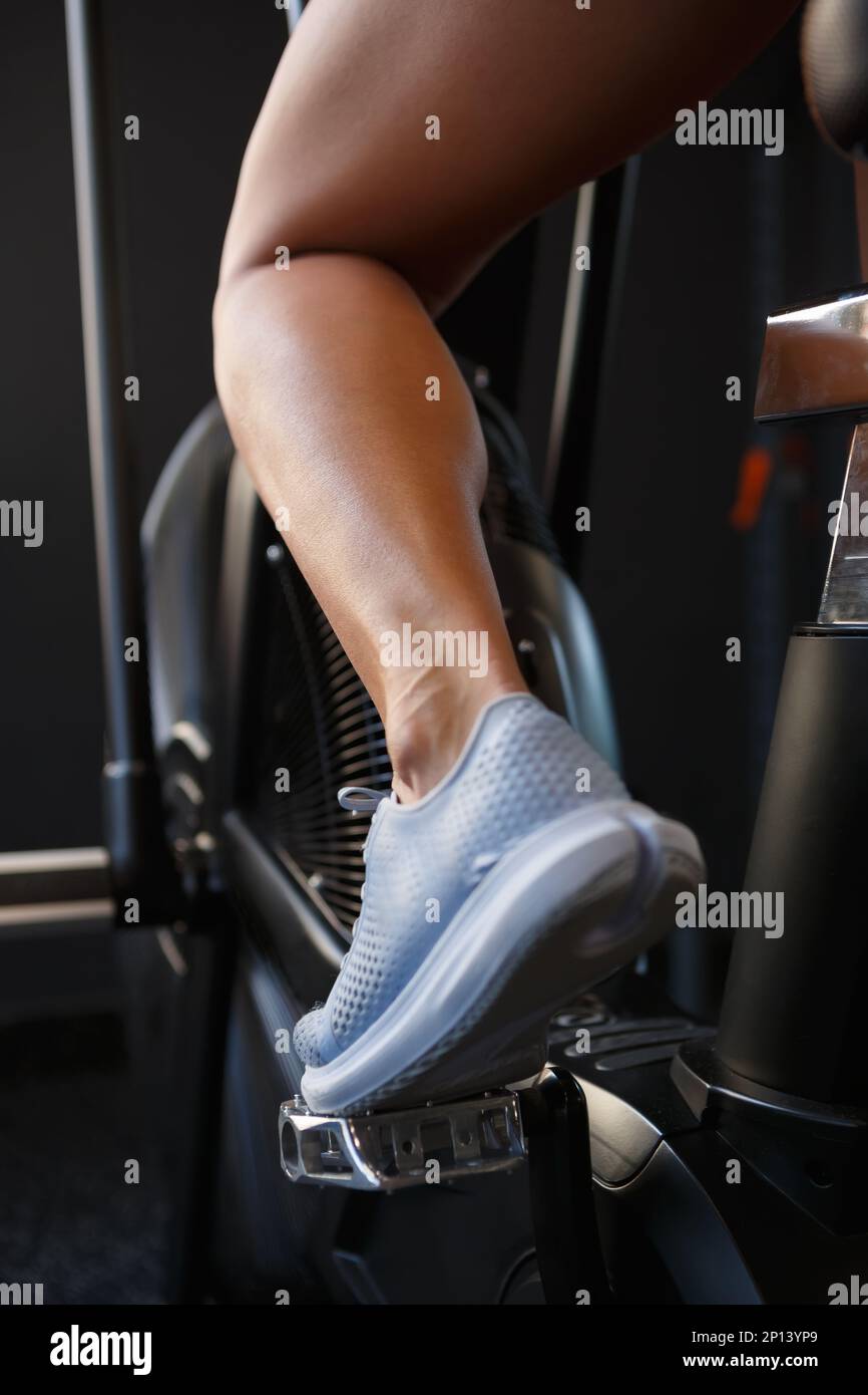 Young woman training on elliptical trainer machine in gym. Close up