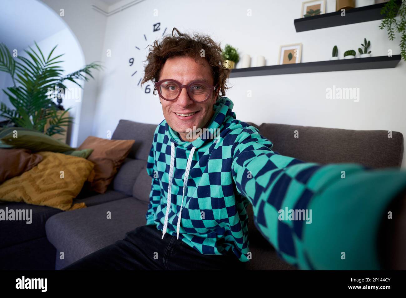 Middle age modern caucasian man taking a selfie at home, sitting on the sofa, looking at camera. Stock Photo