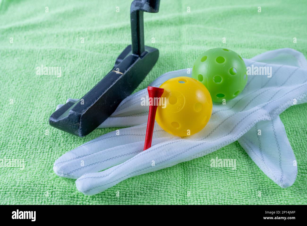 close up of golfing equipment a putter wooden tee and practice balls on green beize with glove for indoor practice Stock Photo