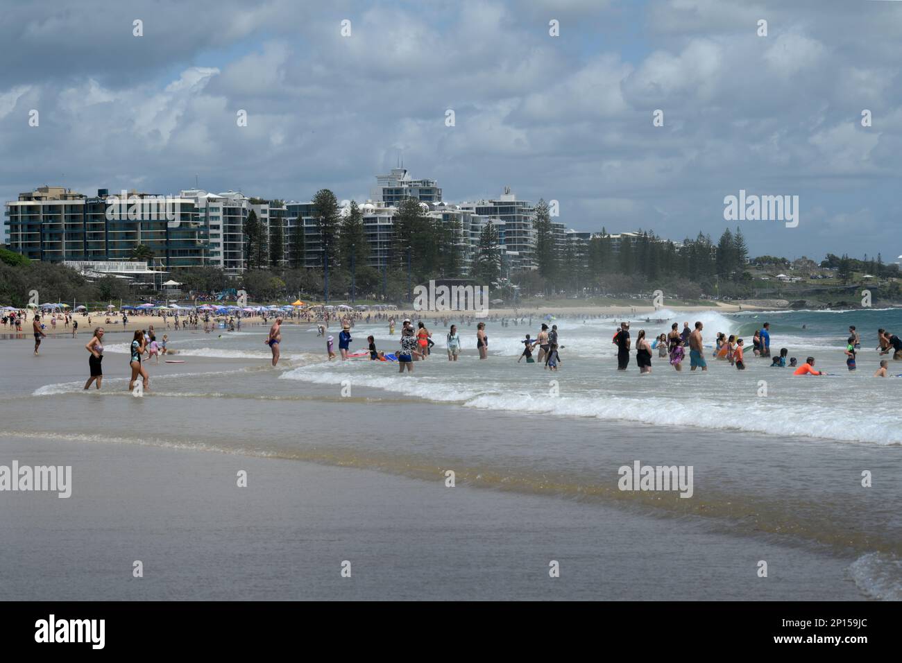 The Beach at Mooloolaba. Swimmers, bodysurfers and sun seekers enjoy the sand and shore waves with beach side apartments on foreshore Stock Photo