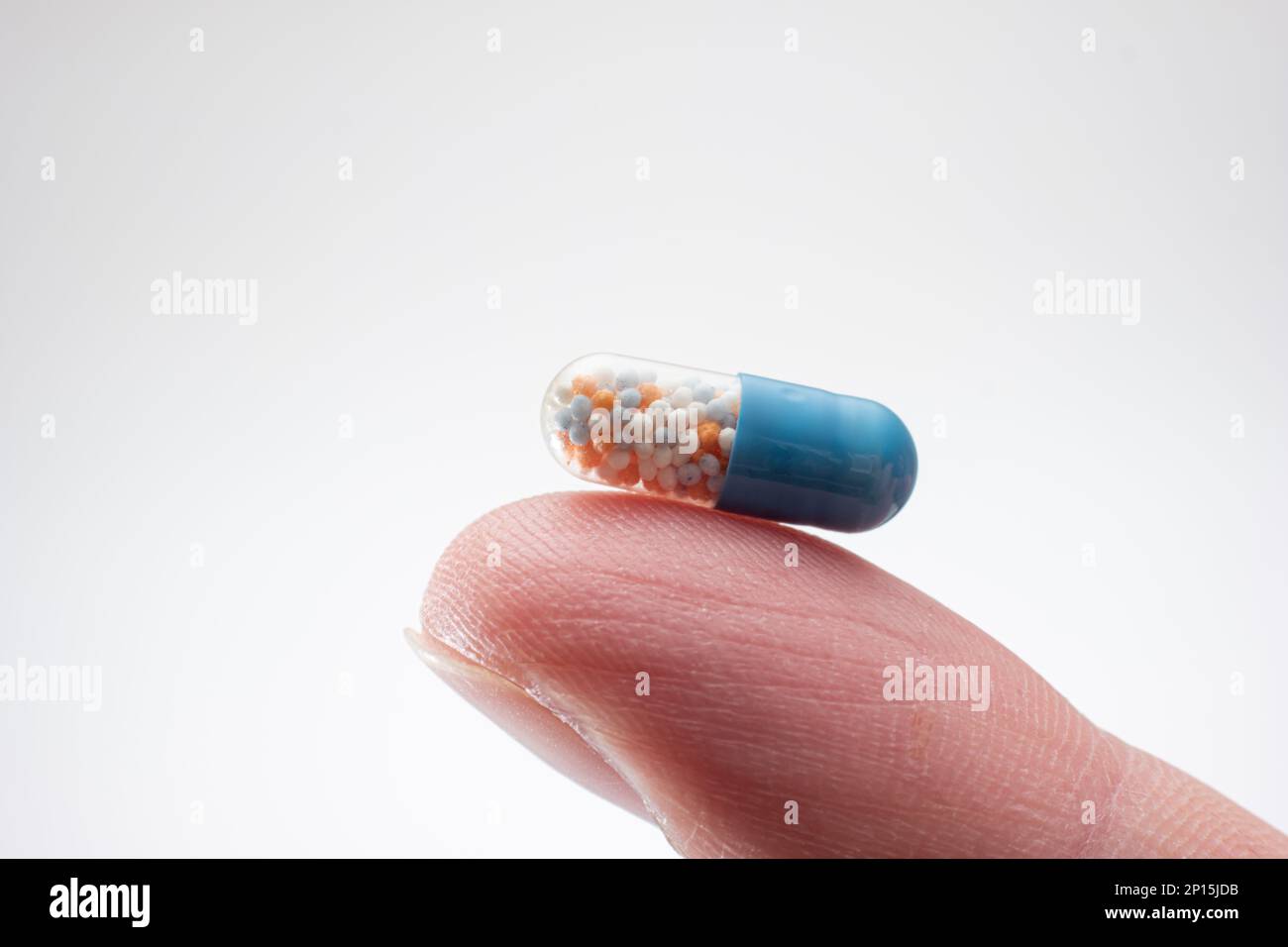 Small medicine medicament capsule half blue half transparent held between fingers. Close up studio macro shot, isolated on white background. Stock Photo