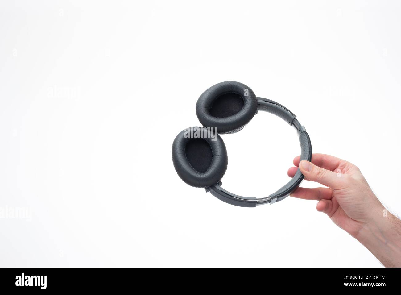 Generic wireless over the ear headphone held in hand by Caucasian male hand. Close up studio shot, isolated on white background. Stock Photo
