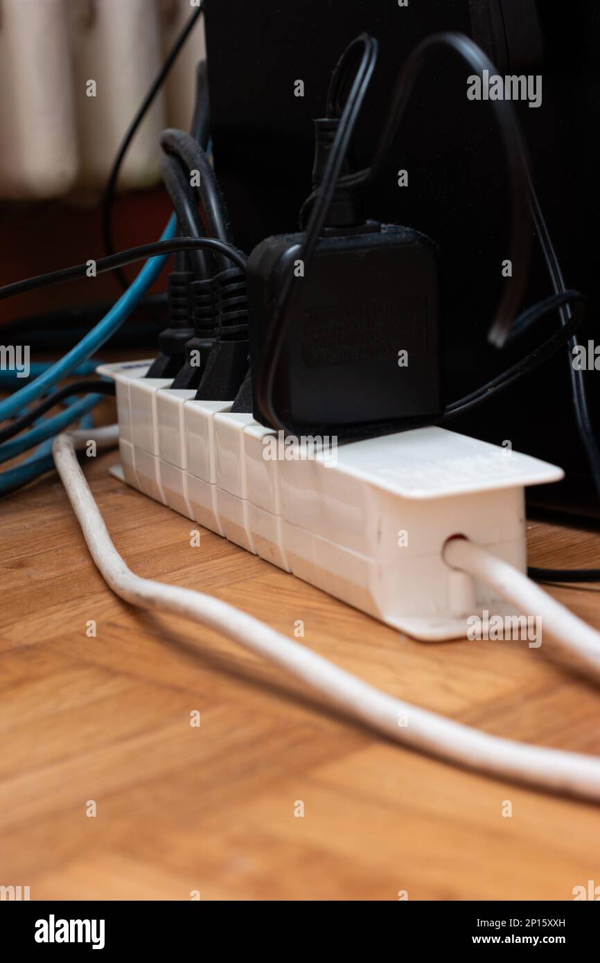 Messy outlet power extension cord on an apartment floor with various charging devices plugged in. Stock Photo