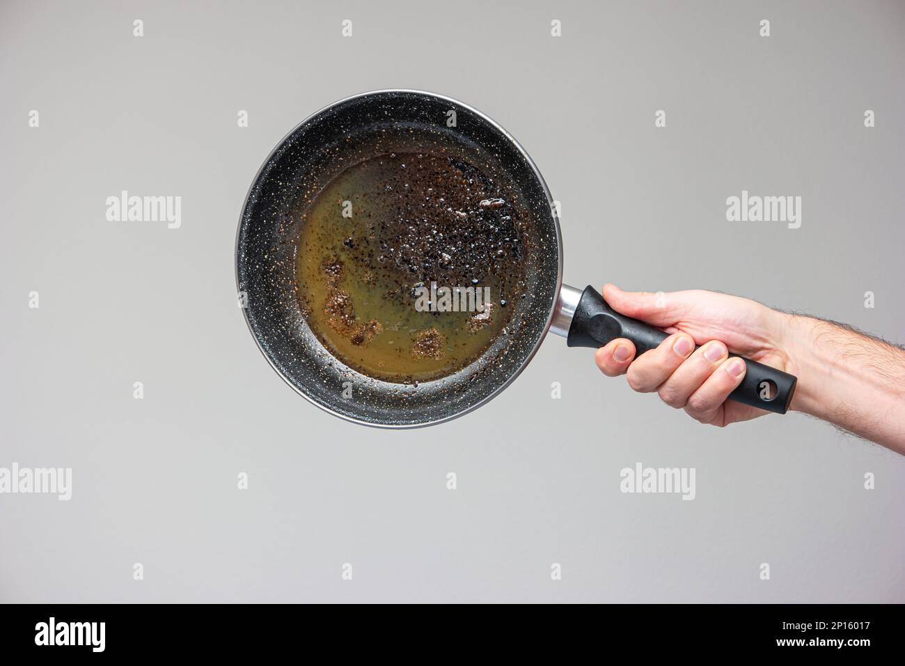 Caucasian male hand holding an old frying pan stained with brown burned