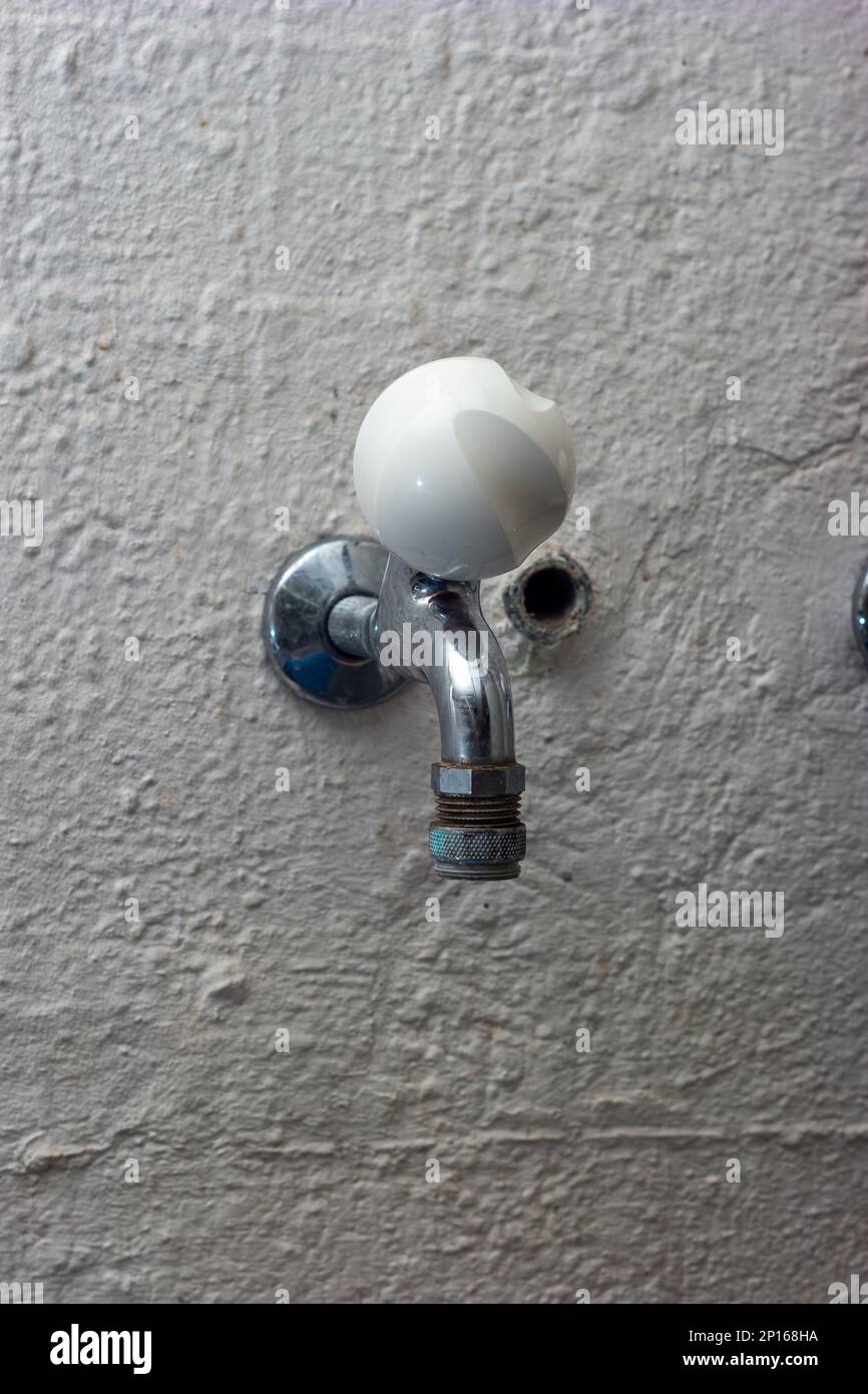 Wall mounted old tap water faucet with white round knob in laundry room