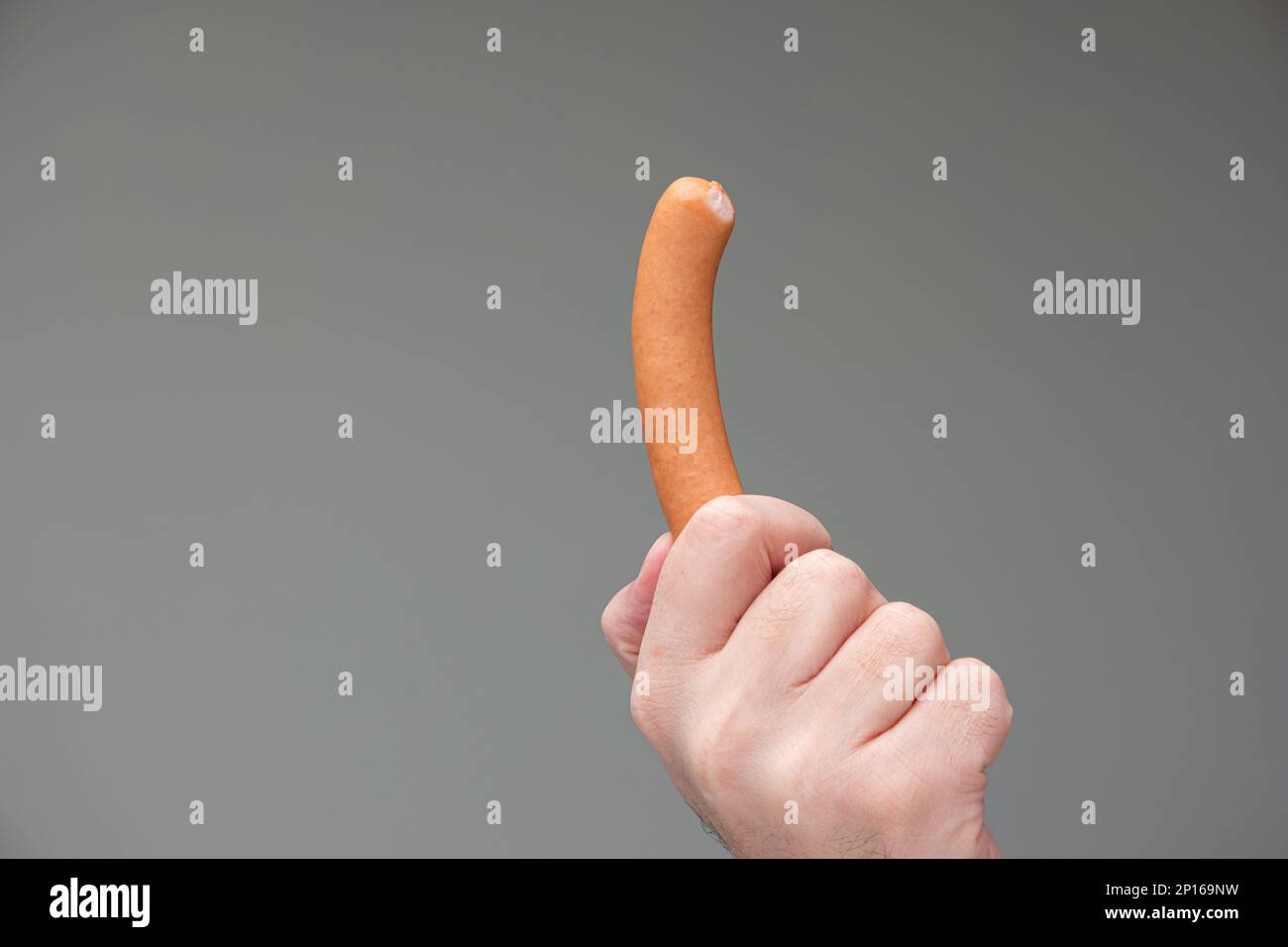 Caucasian male hand holding a bratwurst dog between fingers isolated on gray background. Stock Photo