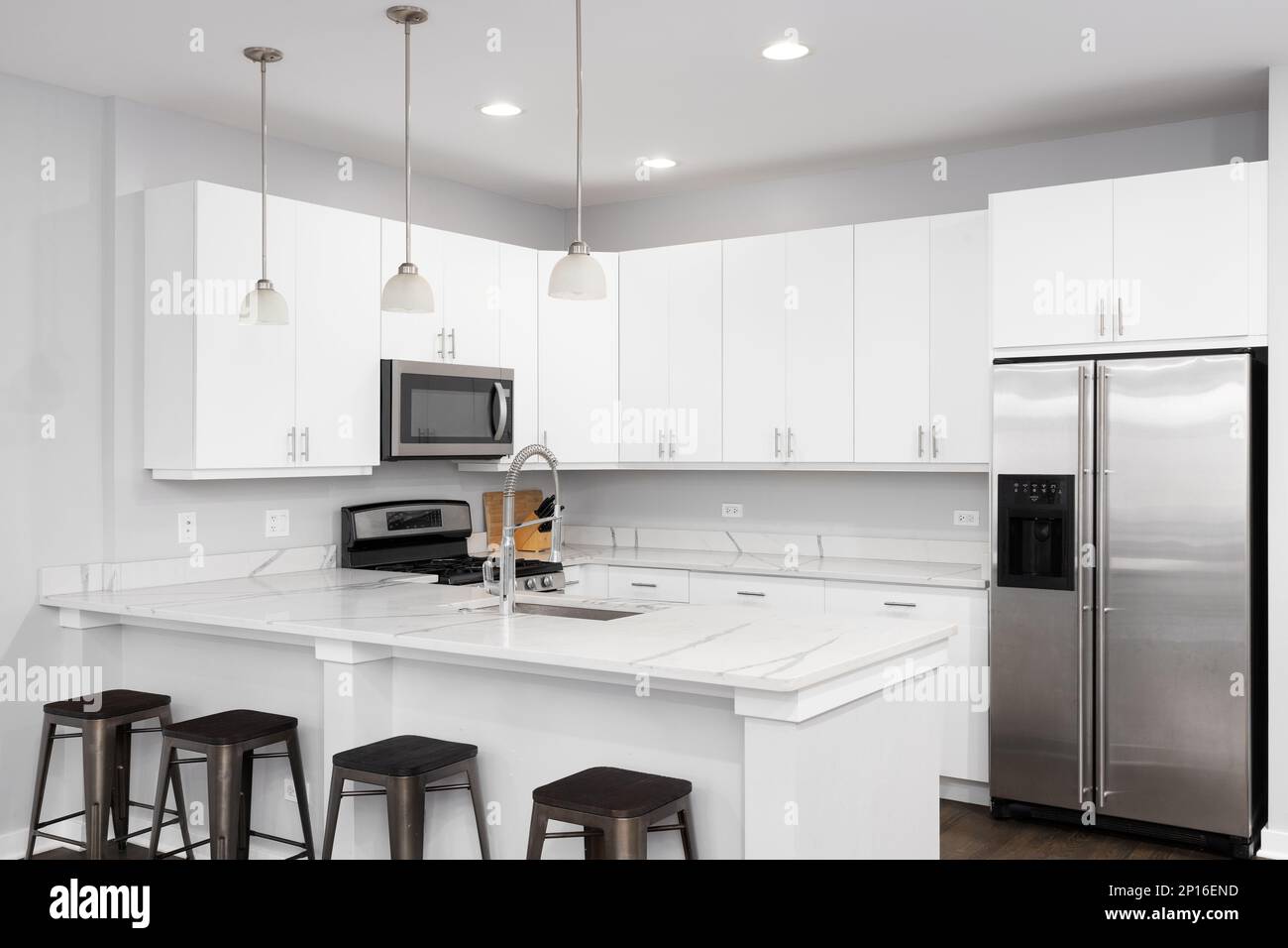 A white kitchen with bar stools sitting at the marble countertop and ...