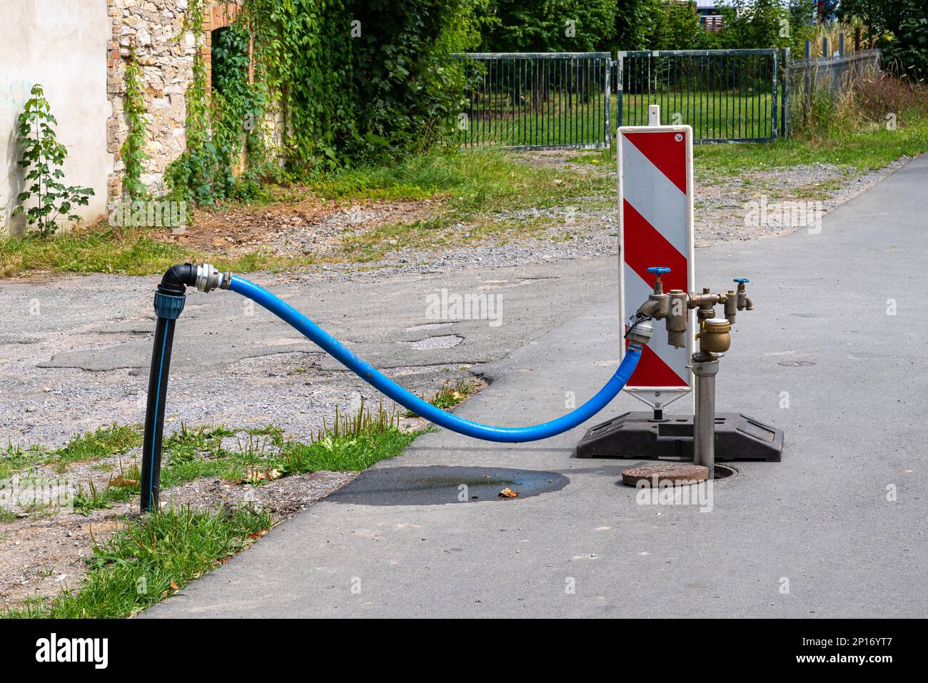 Standpipe with connected blue hose on a pedestrian sidewalk. Red and