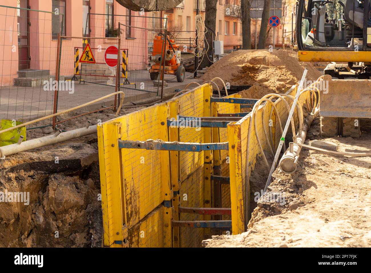 Excavator filling deep excavation supported by trench box with pipe
