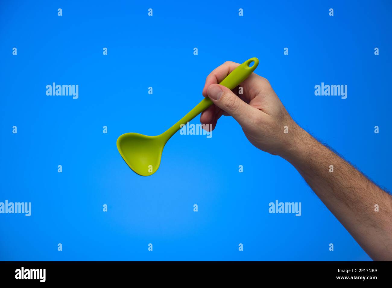 Caucasian male hand holding silicon serving ladle isolated on blue background. Stock Photo