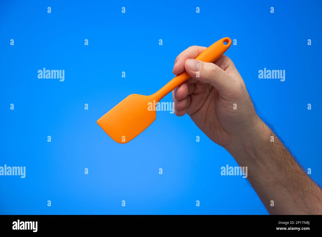Caucasian male hand holding orange silicon spatula isolated on blue background. Stock Photo