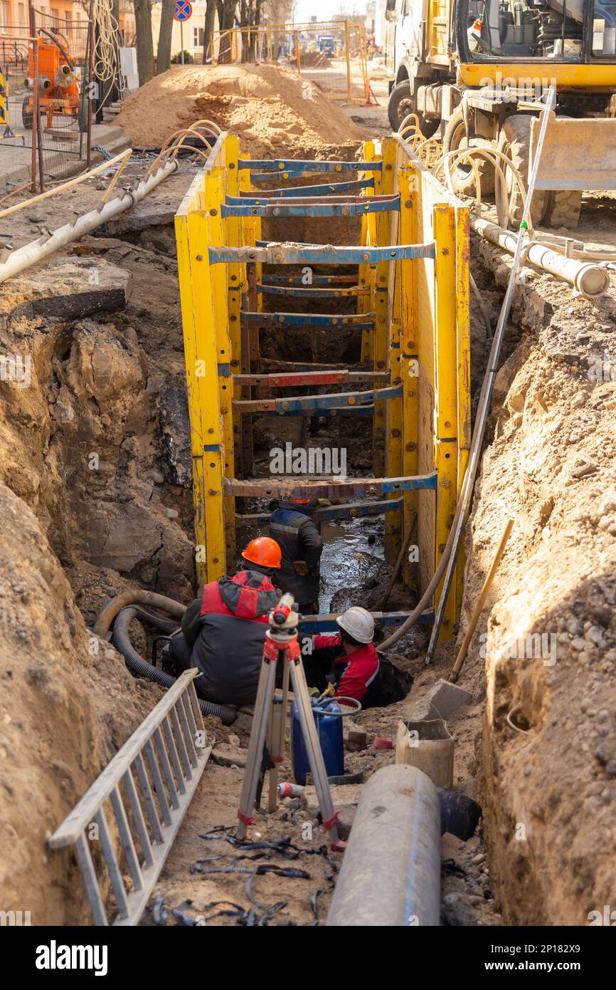 Excavator filling deep excavation supported by trench box with pipe