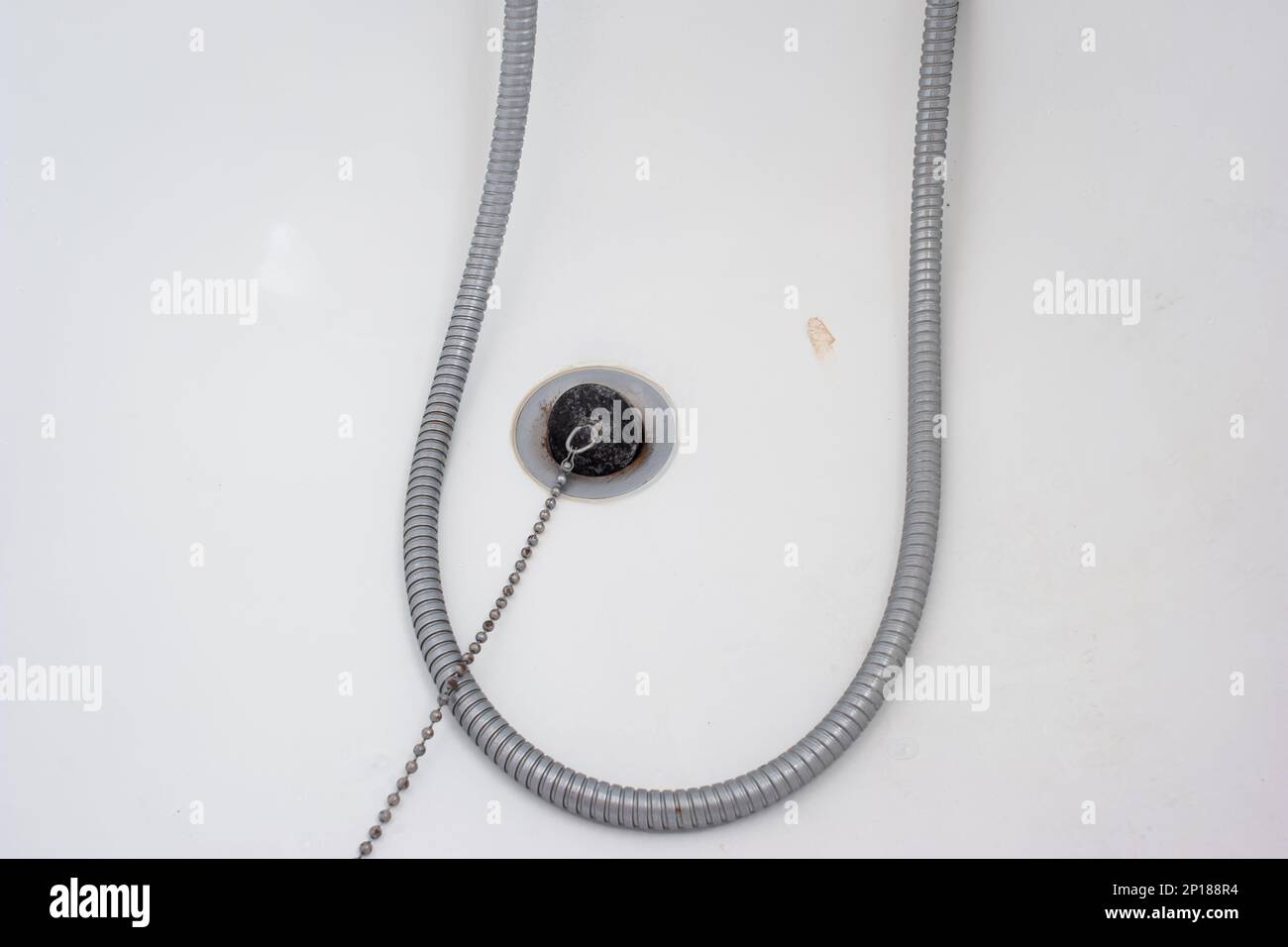 Bathtub rubber plug on a chain next to shower cord close up shot top