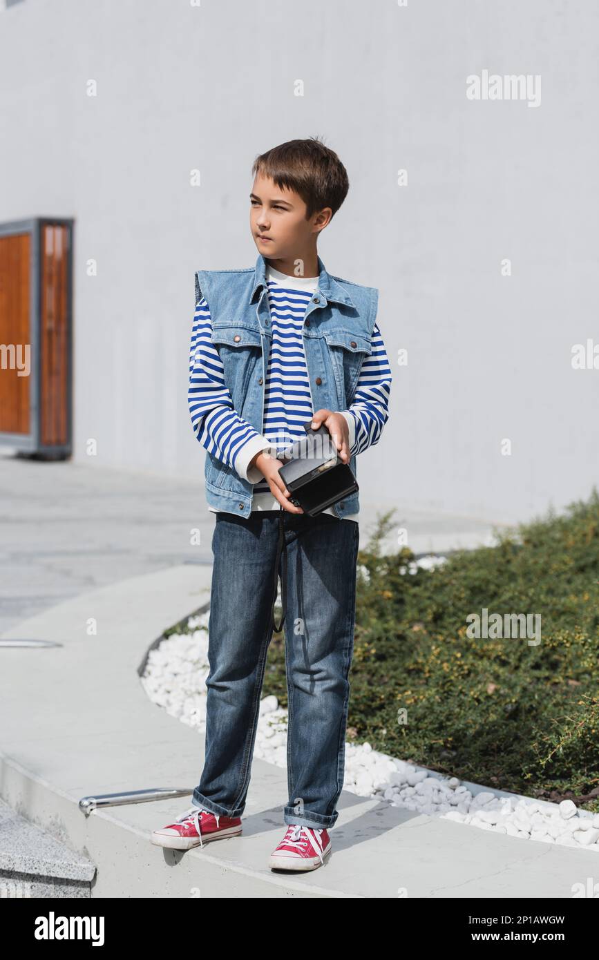 full length of well dressed preteen boy in denim clothes holding vintage camera outside,stock image Stock Photo