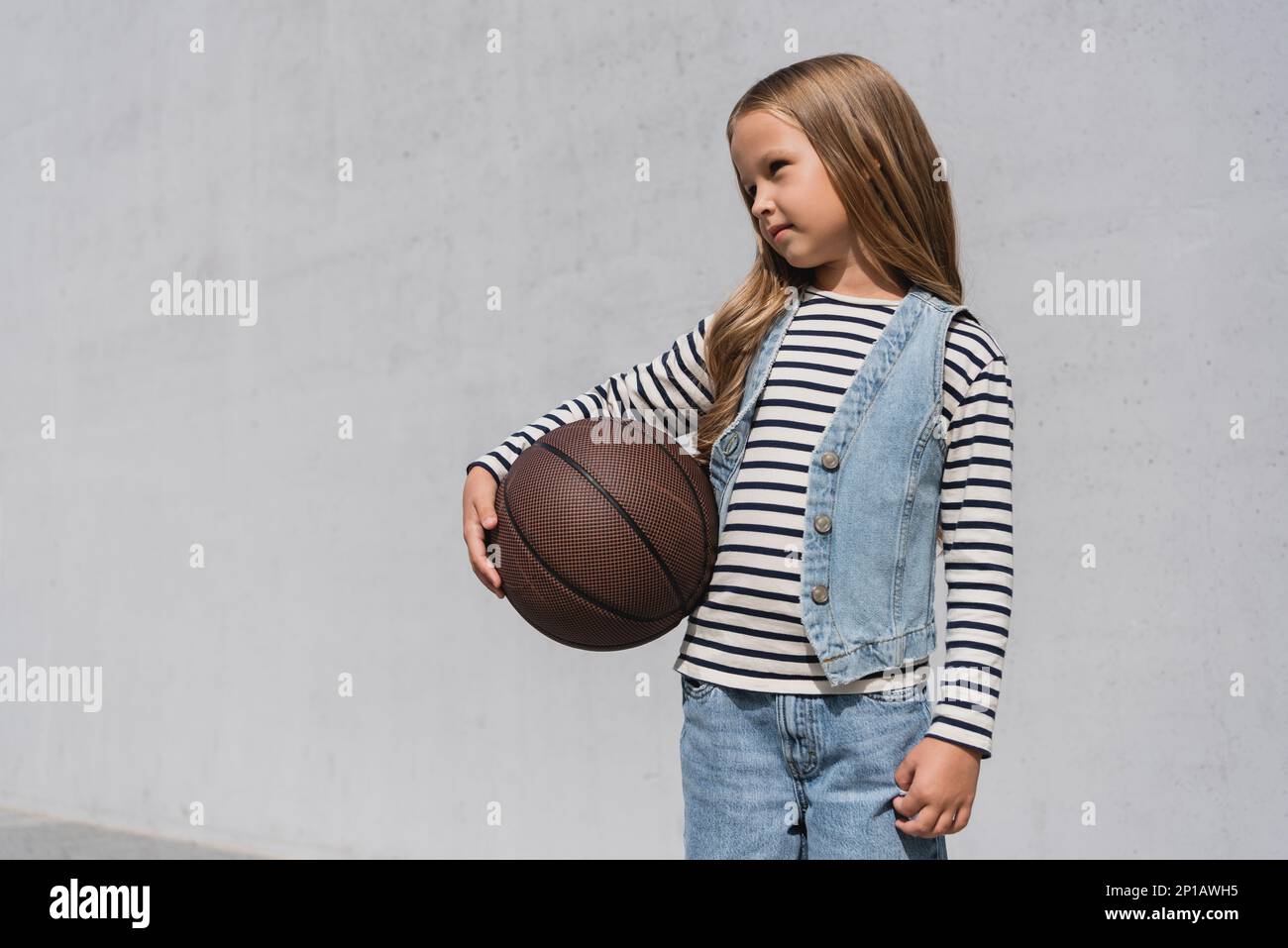 preteen girl in denim vest and blue jeans holding basketball near mall