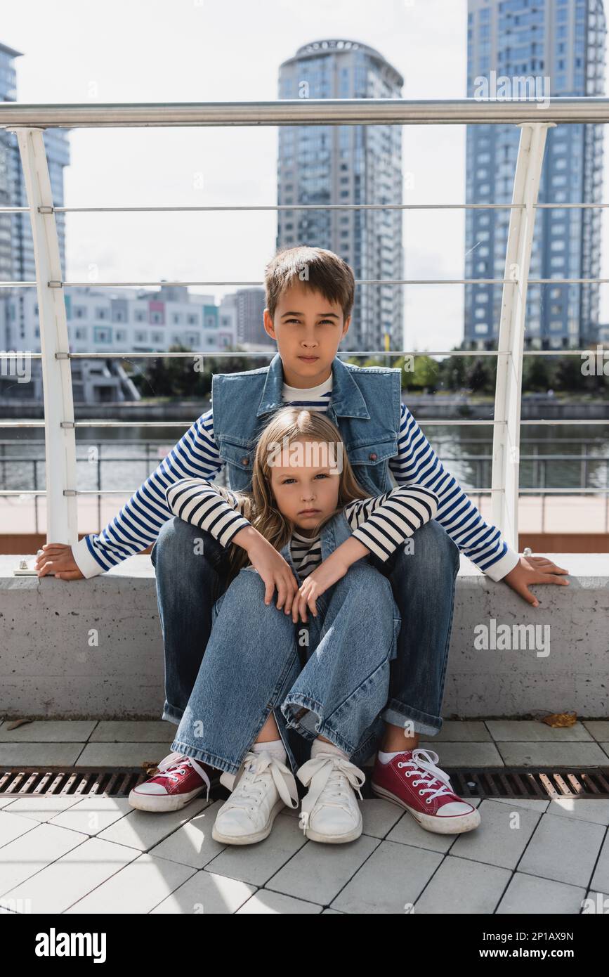 well dressed kids in denim vests and jeans sitting together next to metallic fence on riverside,stock image Stock Photo