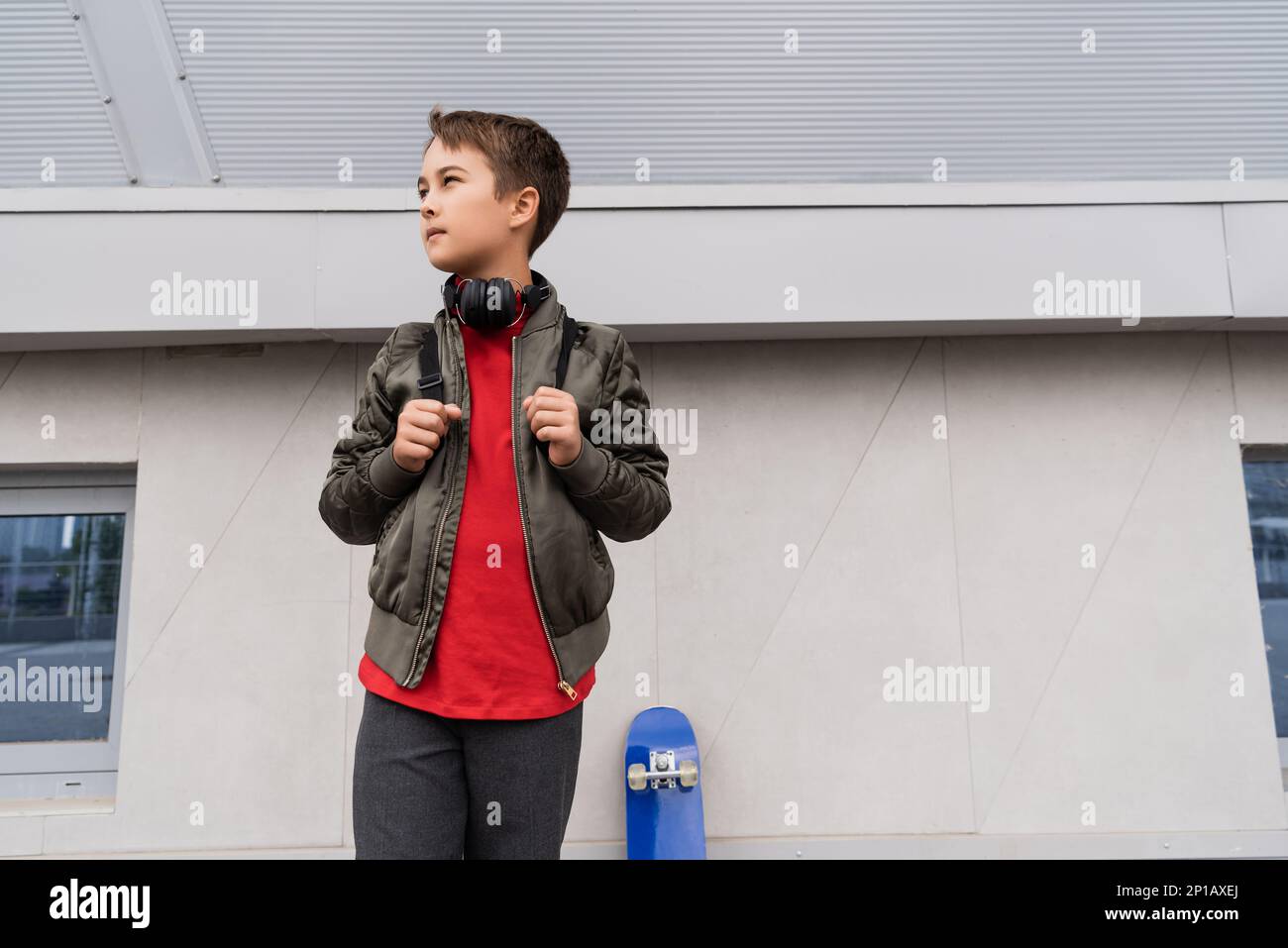 preteen boy in bomber jacket and wireless headphones standing with