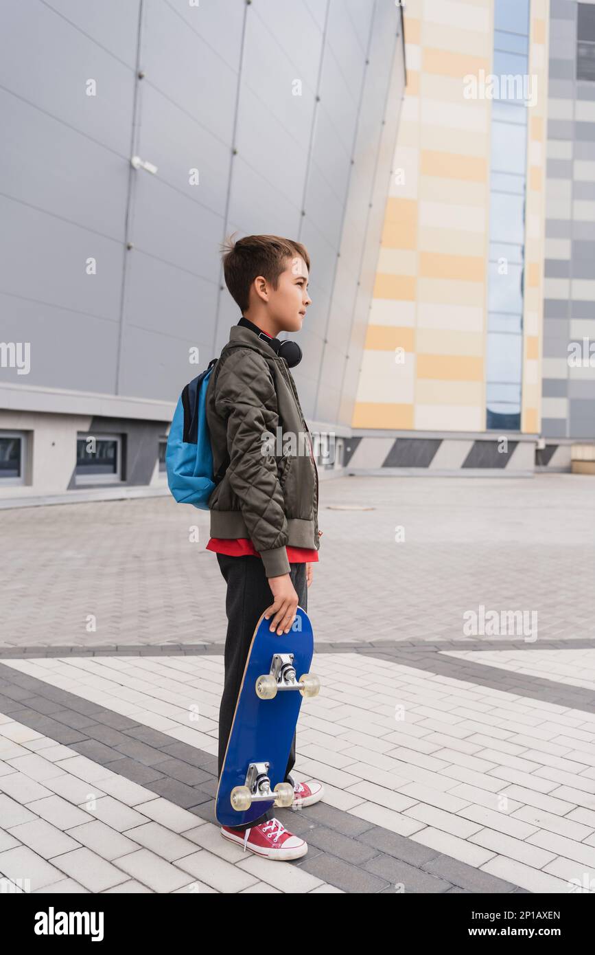 side view of preteen boy in bomber jacket holding penny board while