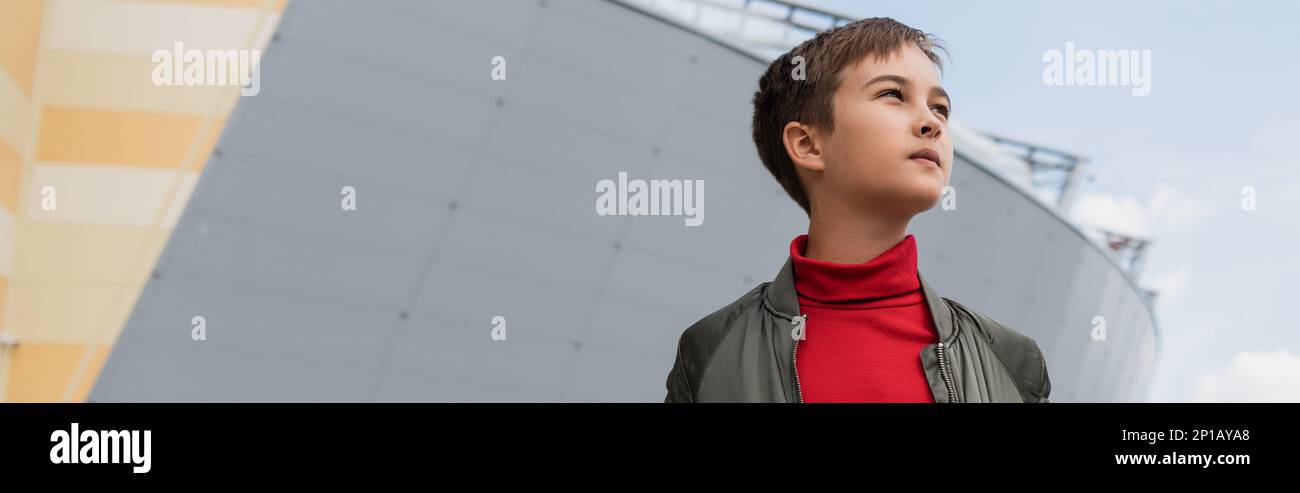 well dressed preteen boy in stylish bomber jacket and red turtleneck looking away near mall, banner,stock image Stock Photo
