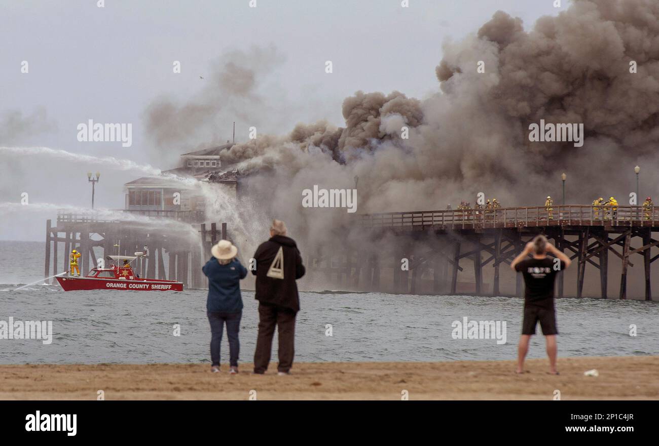 Spectators gather on the sand as fire boats and firefighters battle a ...