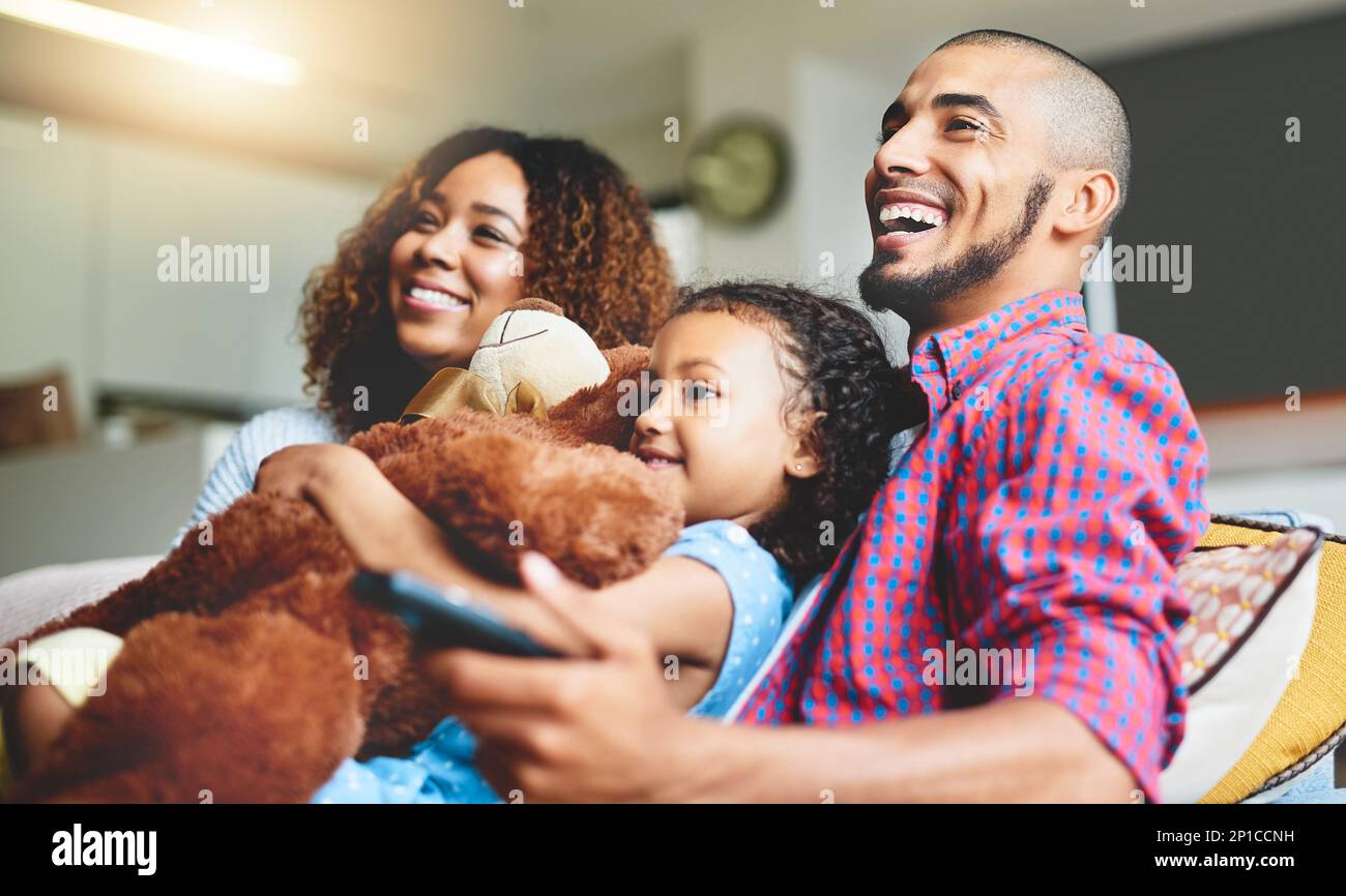Its not movie night without the fam. Shot of a happy young family of three watching tv from the sofa at home. Stock Photo