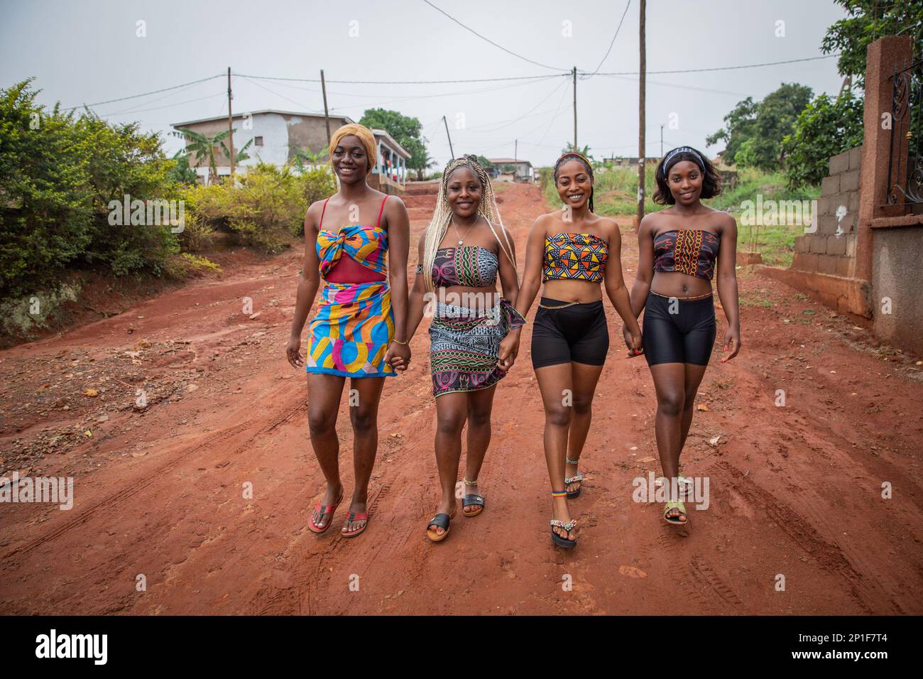 Four young smiling African women walk holding hands, women dressed with traditional African clothes. Stock Photo