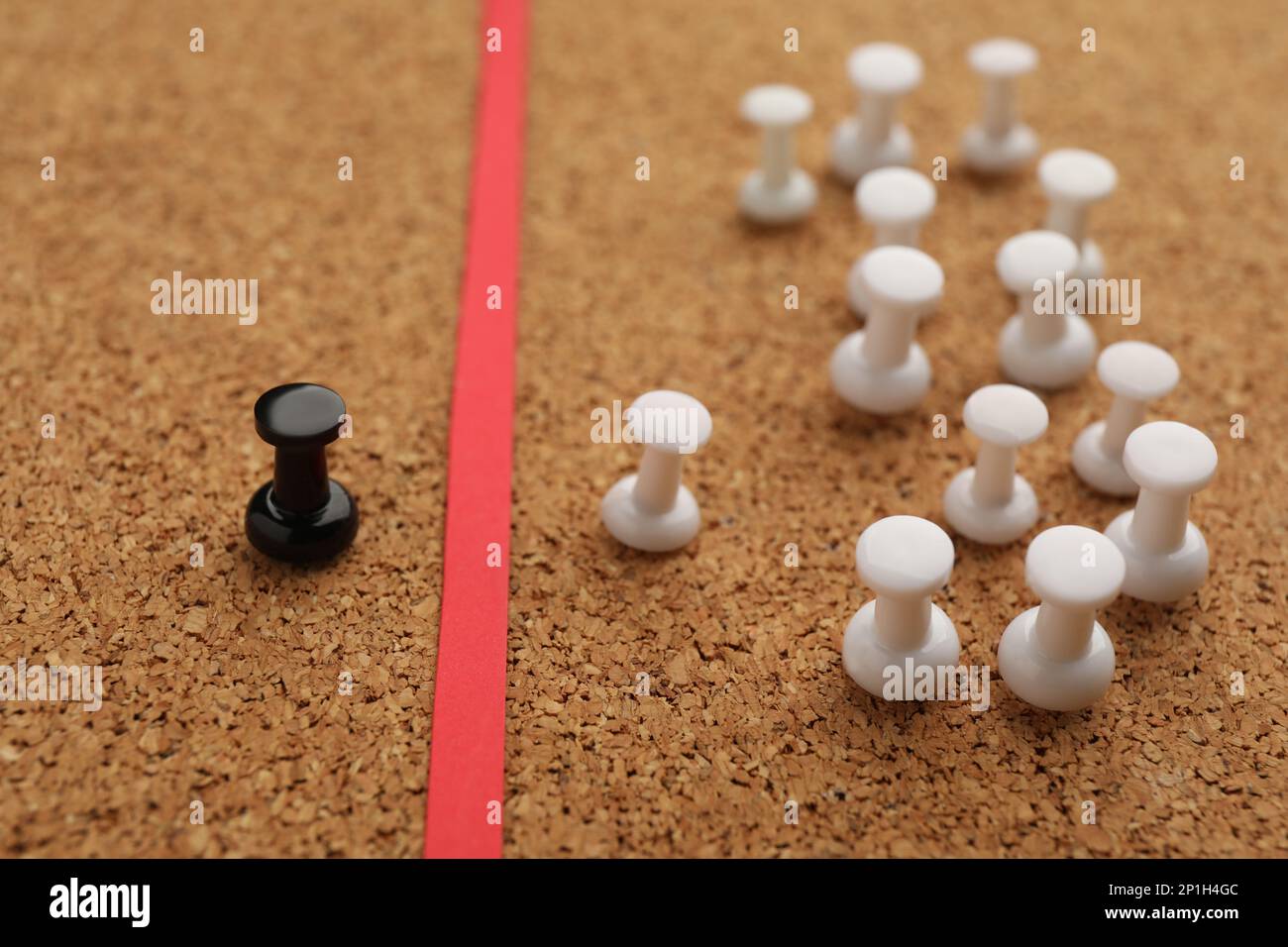 Black push pin separated from white ones by red strip in cork board ...