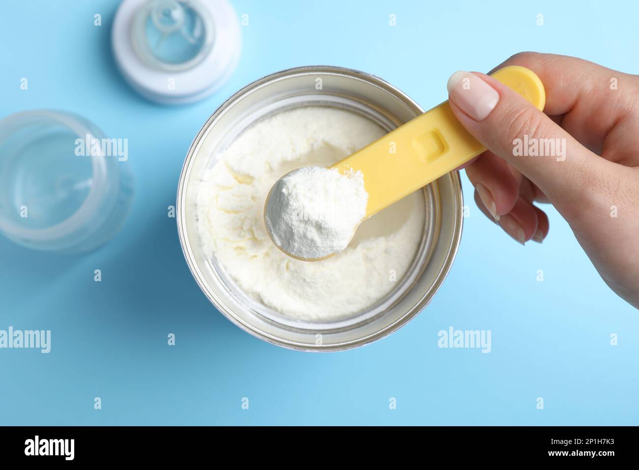 Woman taking powdered infant formula with scoop from can on light blue