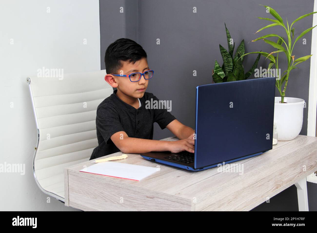 7-year-old Latino boy with glasses does home schooling takes online classes at home on a desk with a laptop, studies, is surprised Stock Photo