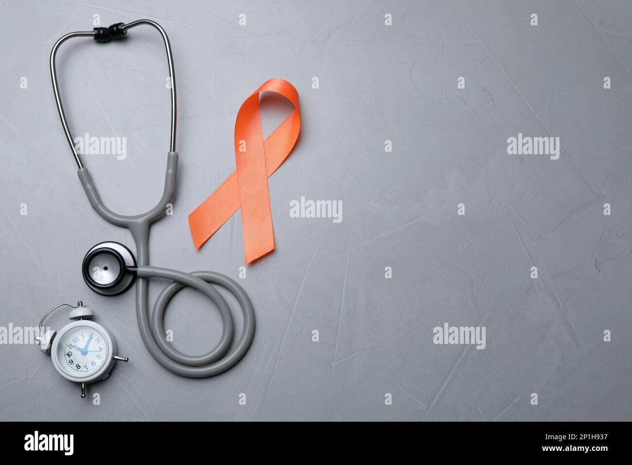 Orange ribbon, stethoscope and alarm clock on light grey table, flat lay with space for text. Multiple sclerosis awareness Stock Photo