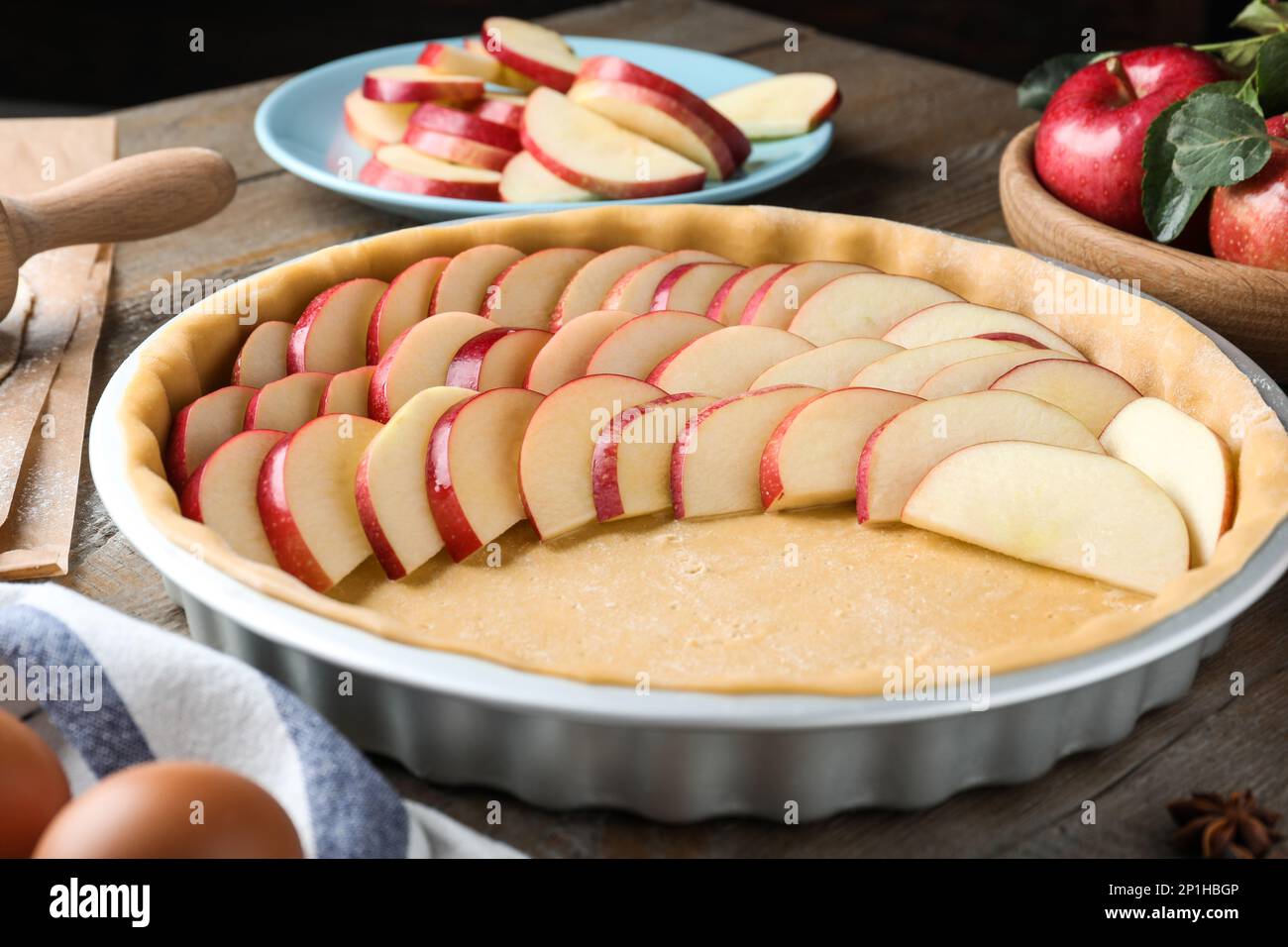 Dish with fresh apple slices and raw dough on wooden table. Baking pie Stock Photo