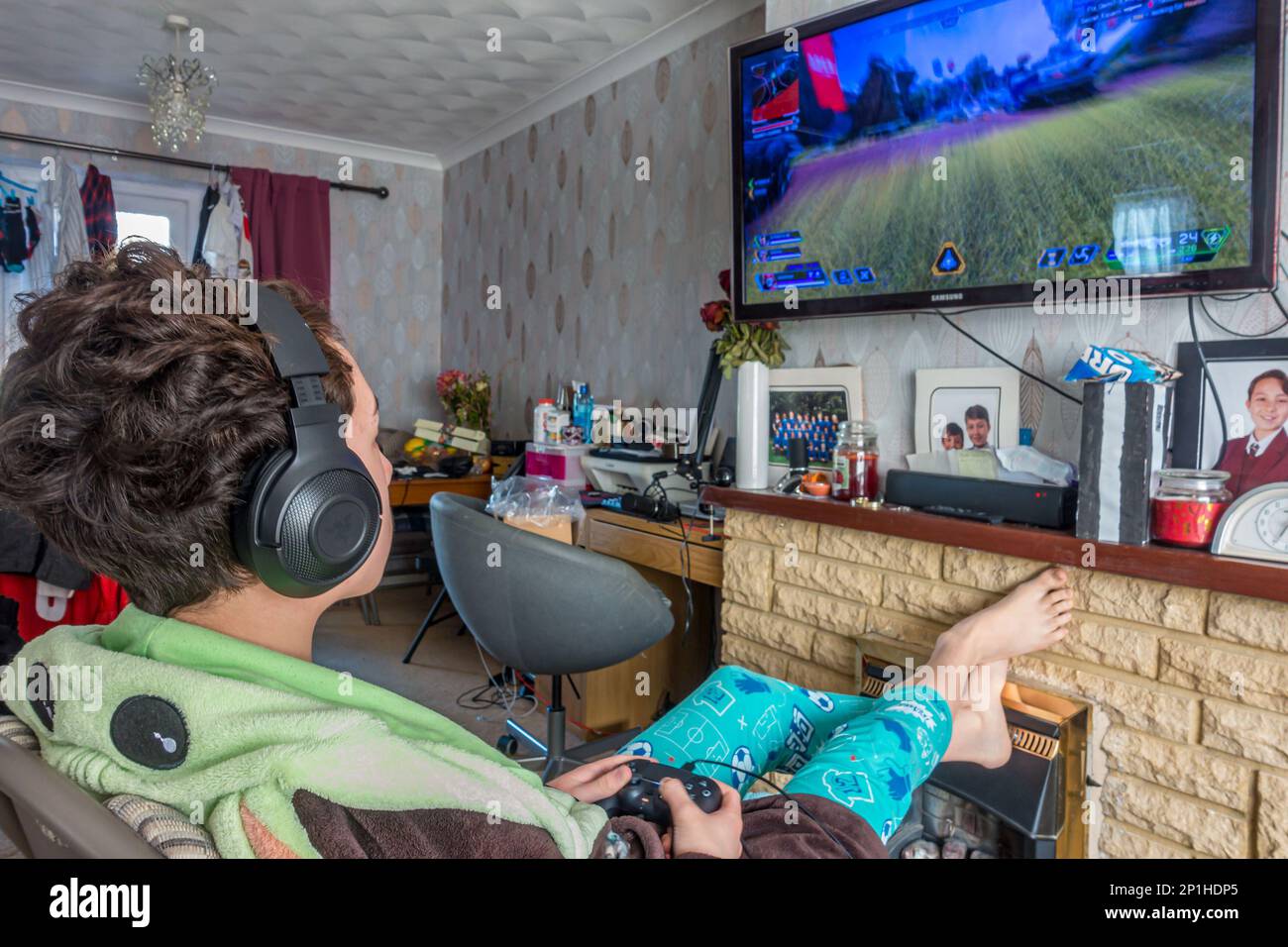 A teenage boy playing the APEX Legends video game on a gaming console attached to a television in the lounge Stock Photo