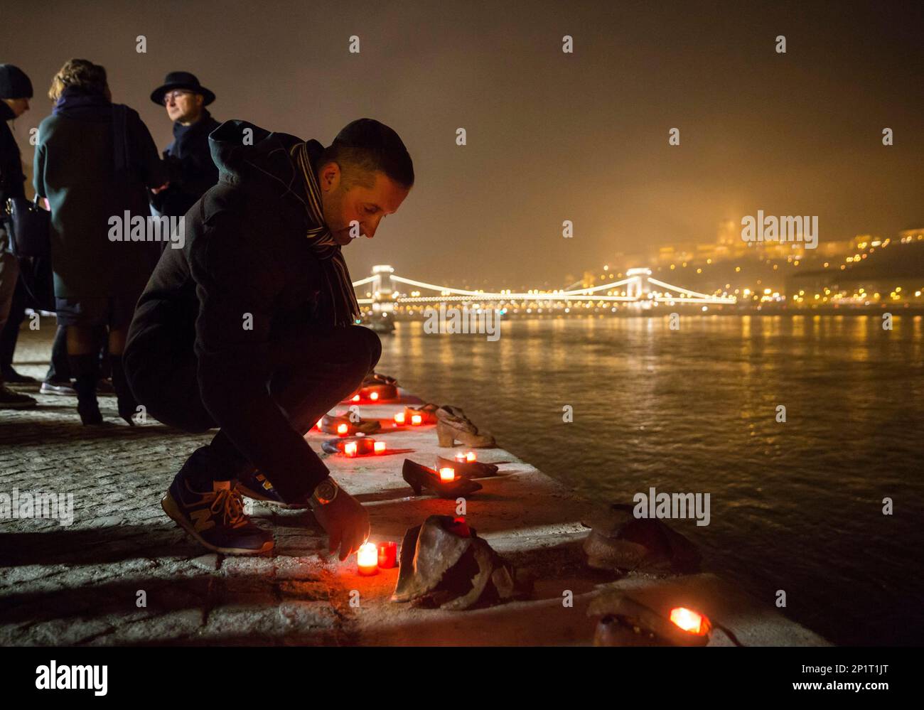 Backdropped by the illuminated Chain Bridge, people light candles in