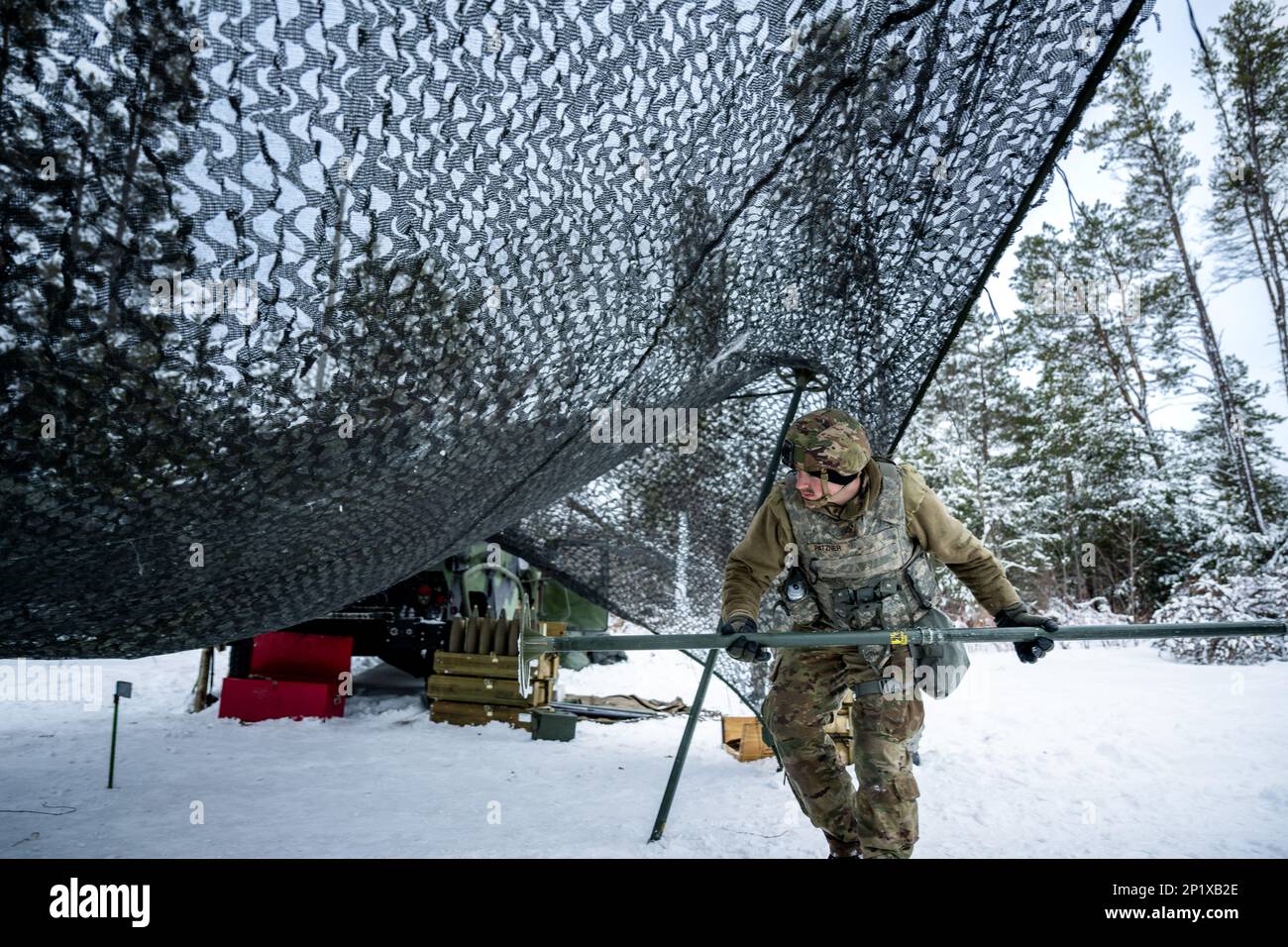 Army Sgt. Trayton Pankratz, 1-120th Field Artillery Regiment, uses a pole to raise a camouflage canopy while setting up an M119 howitzer during Northern Strike 23-1, Jan. 25, 2023, at Camp Grayling, Mich. Units that participate in Northern Strike’s winter iteration build readiness by conducting joint, cold-weather training designed to meet objectives of the Department of Defense’s Arctic Strategy. Stock Photo