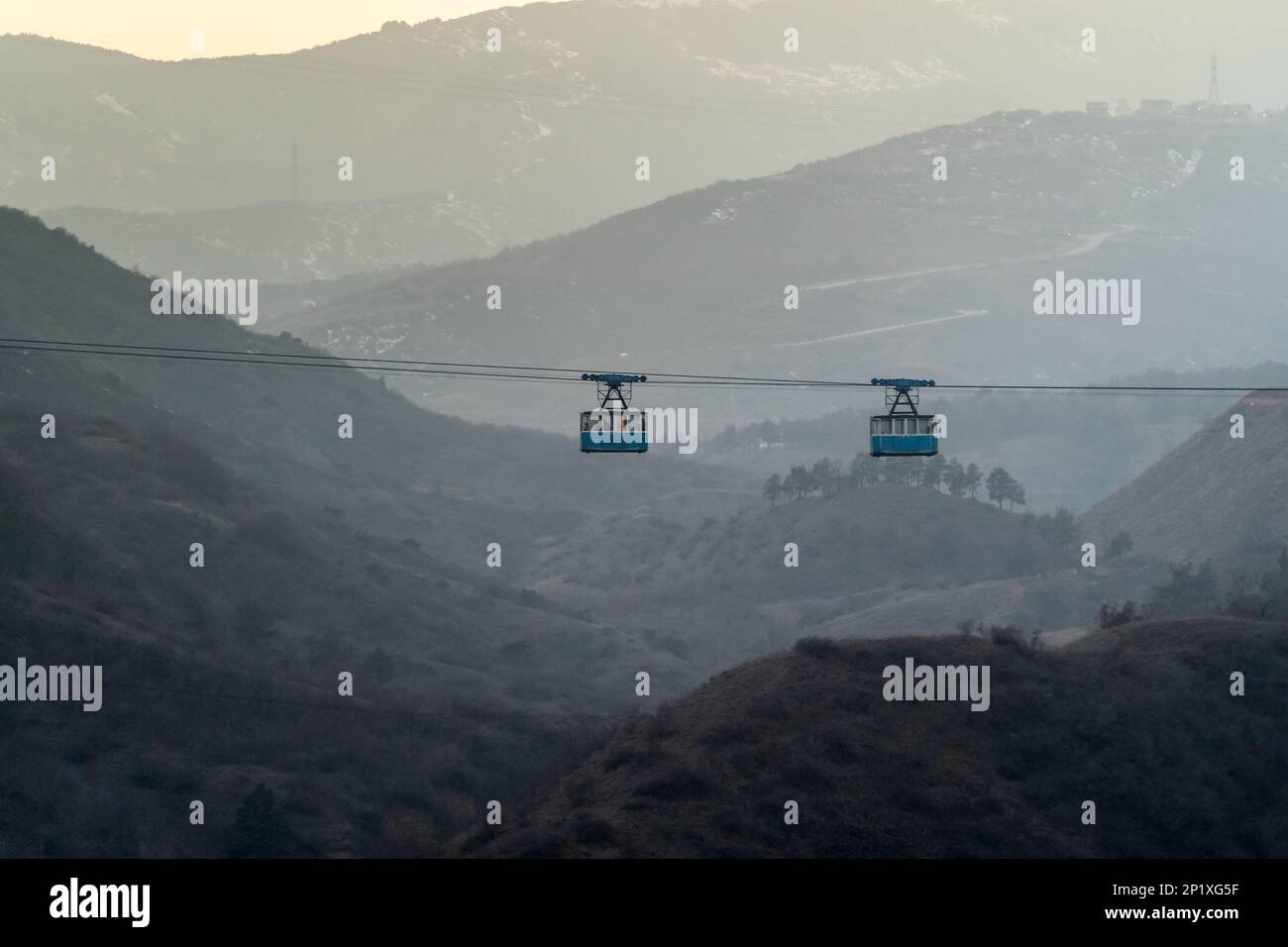 Two blue public old cabins of cable car moves against backdrop of misty ...