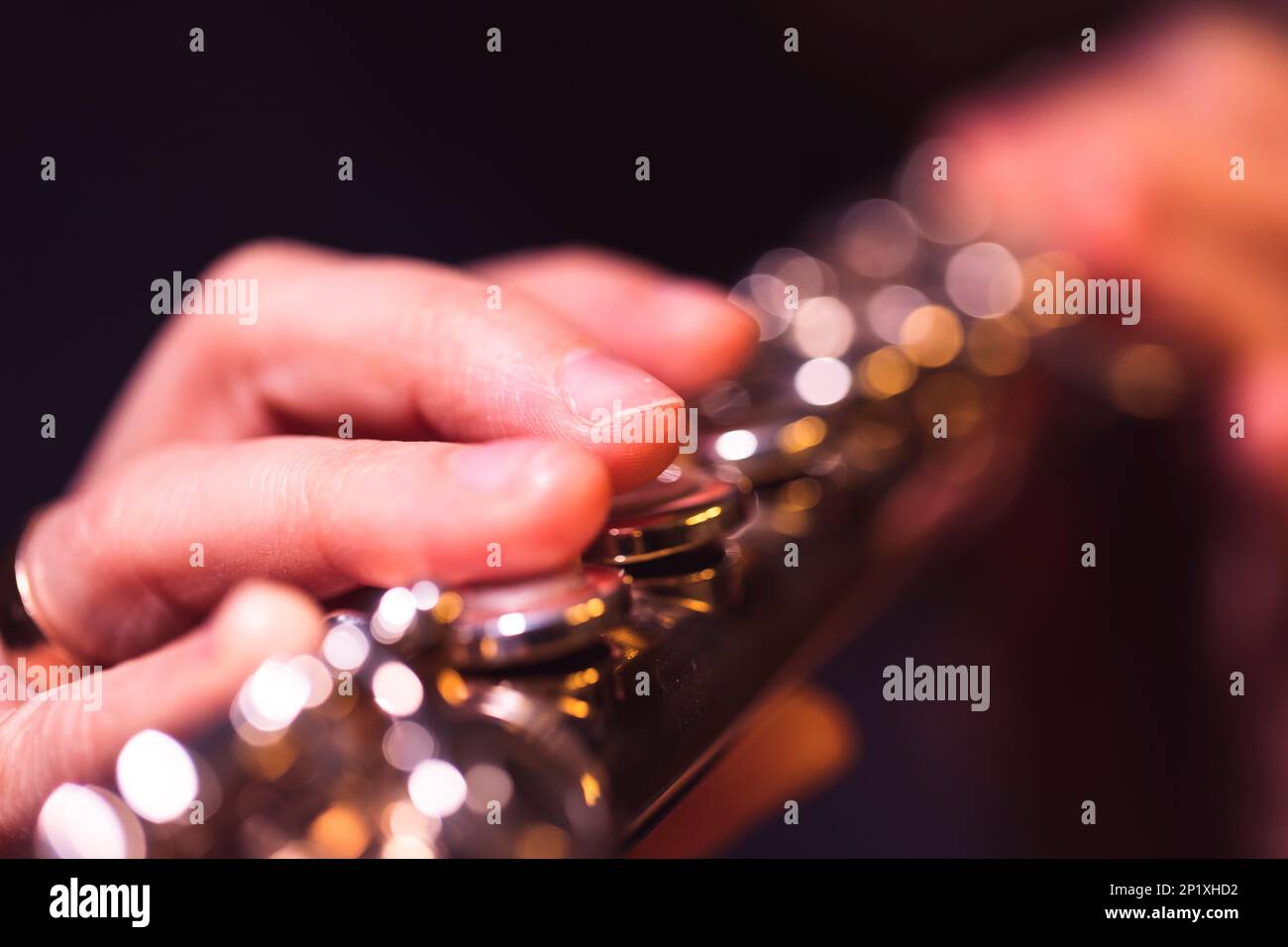 A close up portrait of fingers pressing down on the metal valves of a silver flute by a flutist