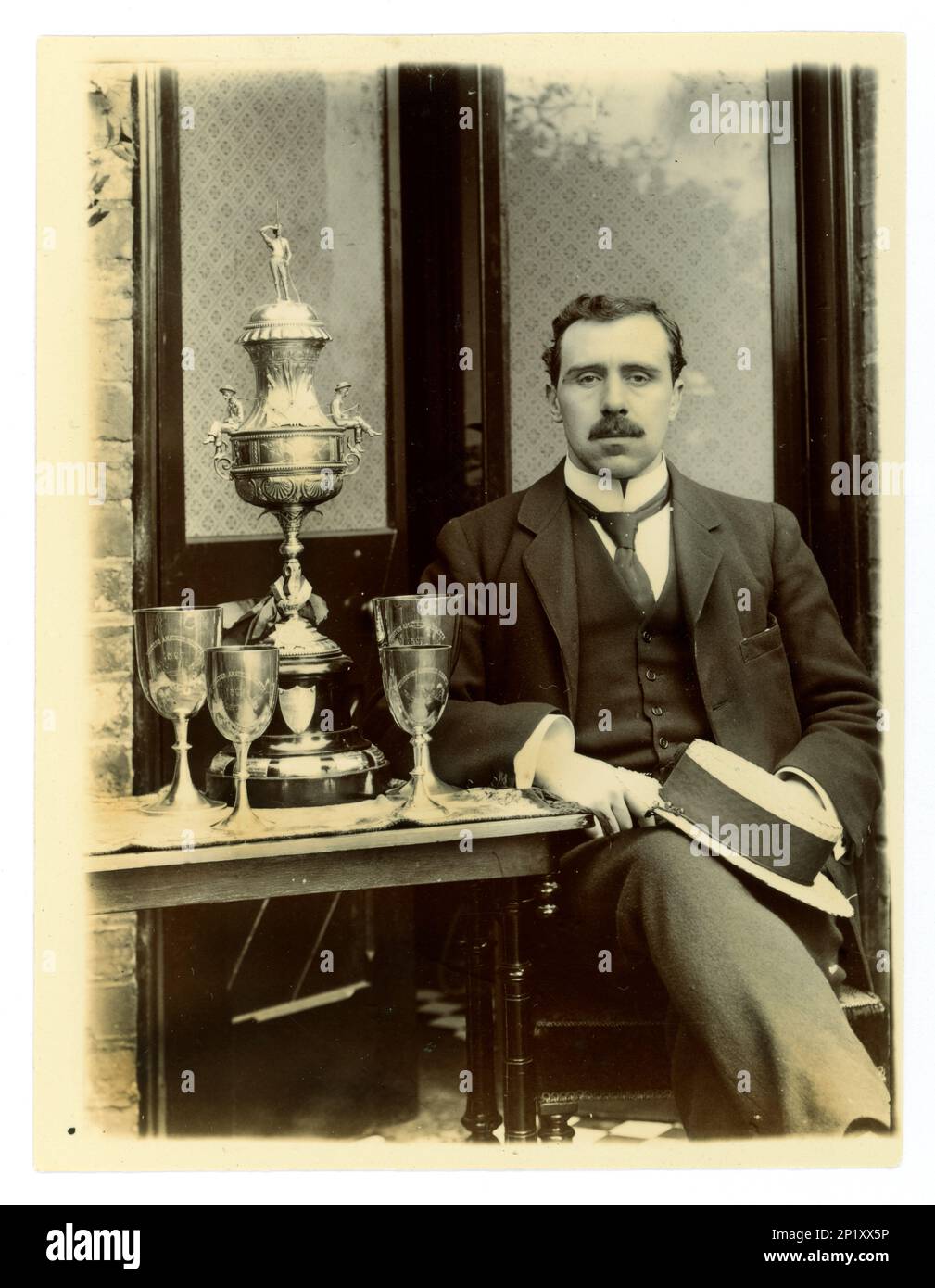 Original Victorian photograph of gent, holding a boater. Next to him on a table there is displayed a large Worcester challenge vase, / regatta trophy for rowing, and other cups,  Possibly member of a coxed four crew. Worcester area, U.K.  circa 1897-1899 Stock Photo