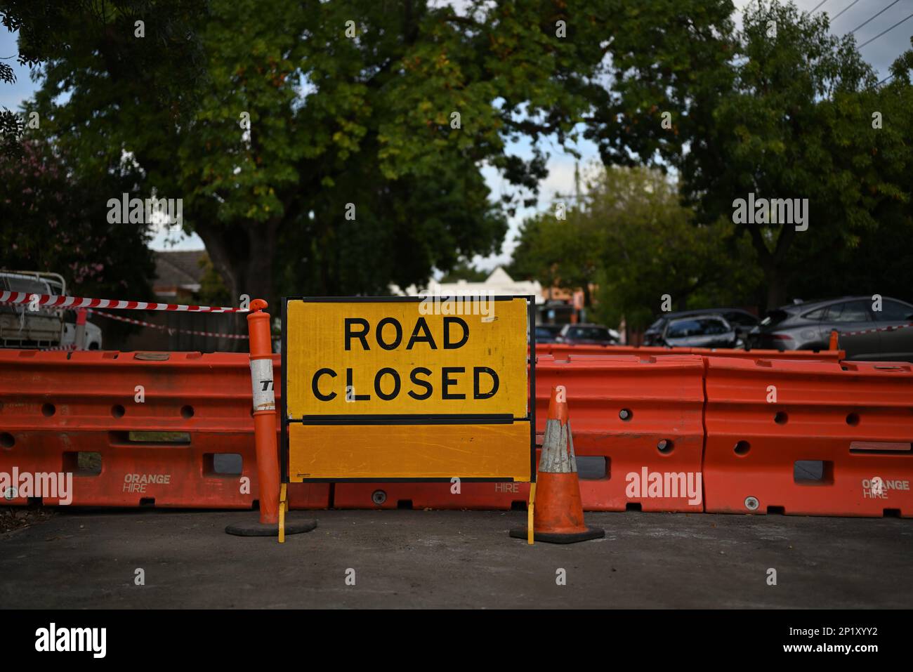 Yellow road closed sign in front of orange barriers in a leafy suburban Melbourne street Stock Photo