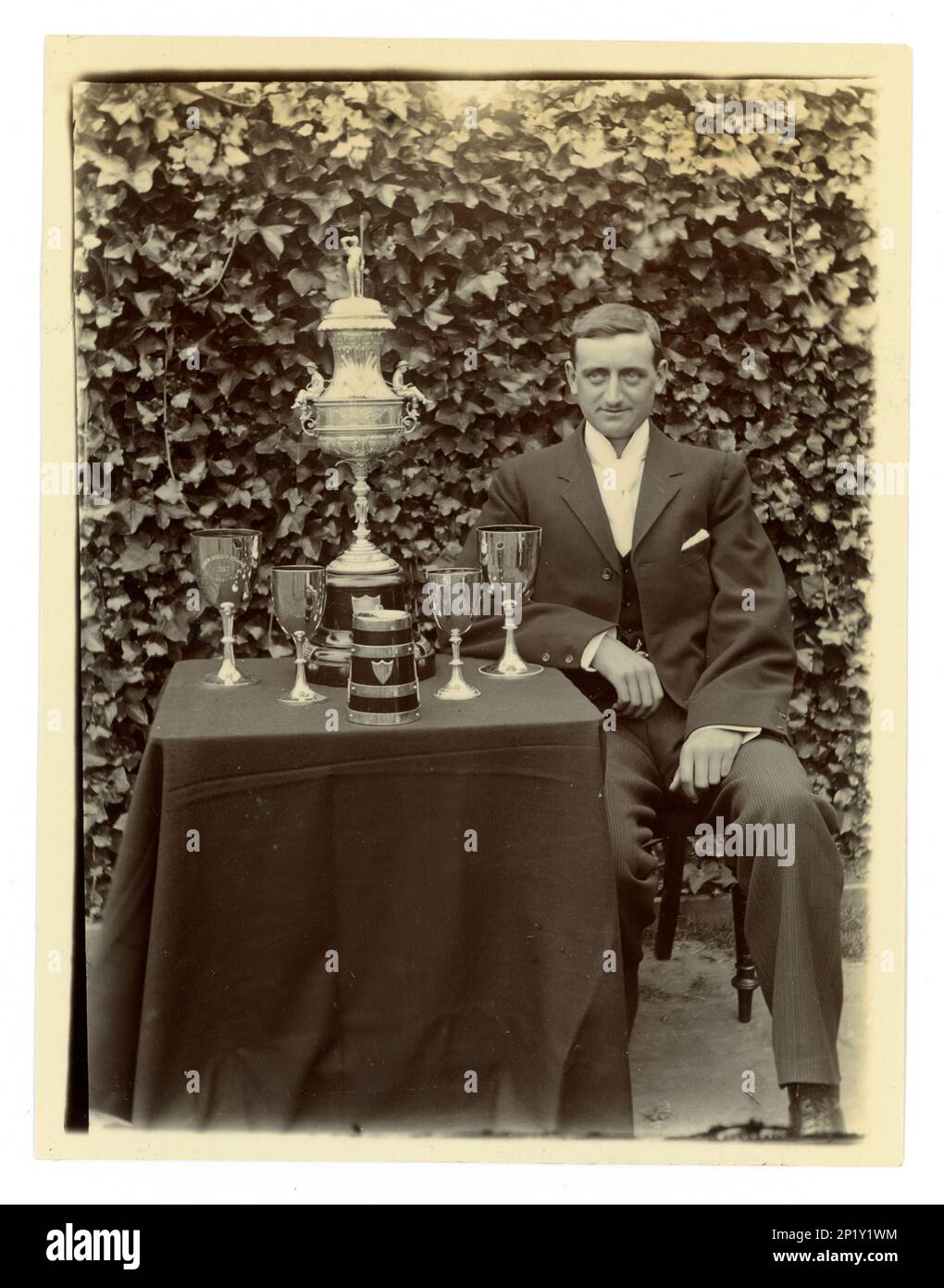 Original Victorian photograph of gent, on a table there is displayed a large Worcester challenge vase, / regatta trophy for rowing, and other cups,  Possibly member of a coxed four crew. Worcester area, U.K.  circa 1897-1899 Stock Photo