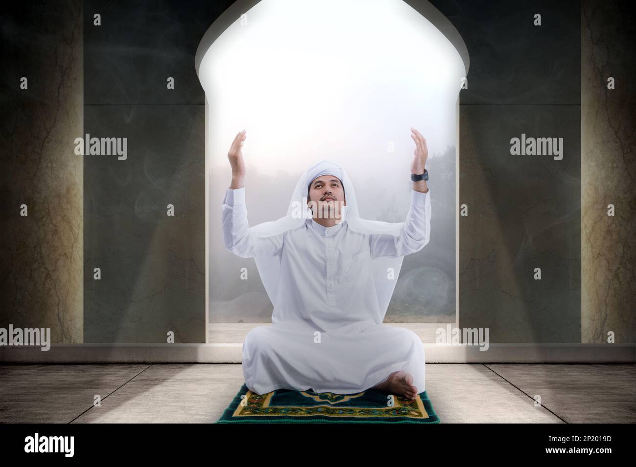 Muslim man sitting while raised hands and praying in the mosque Stock Photo