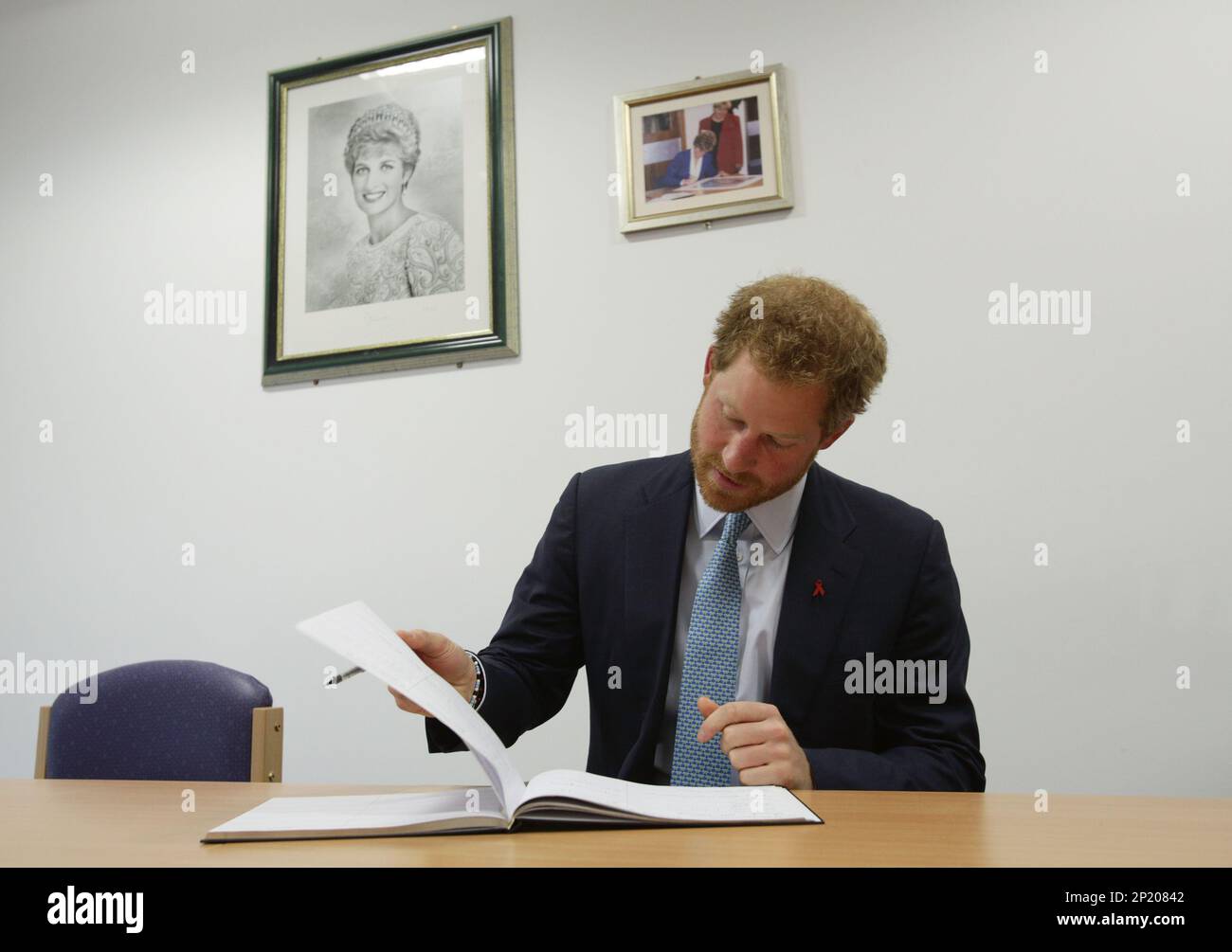 Britain's Prince Harry signs the visitors book, with photos of his