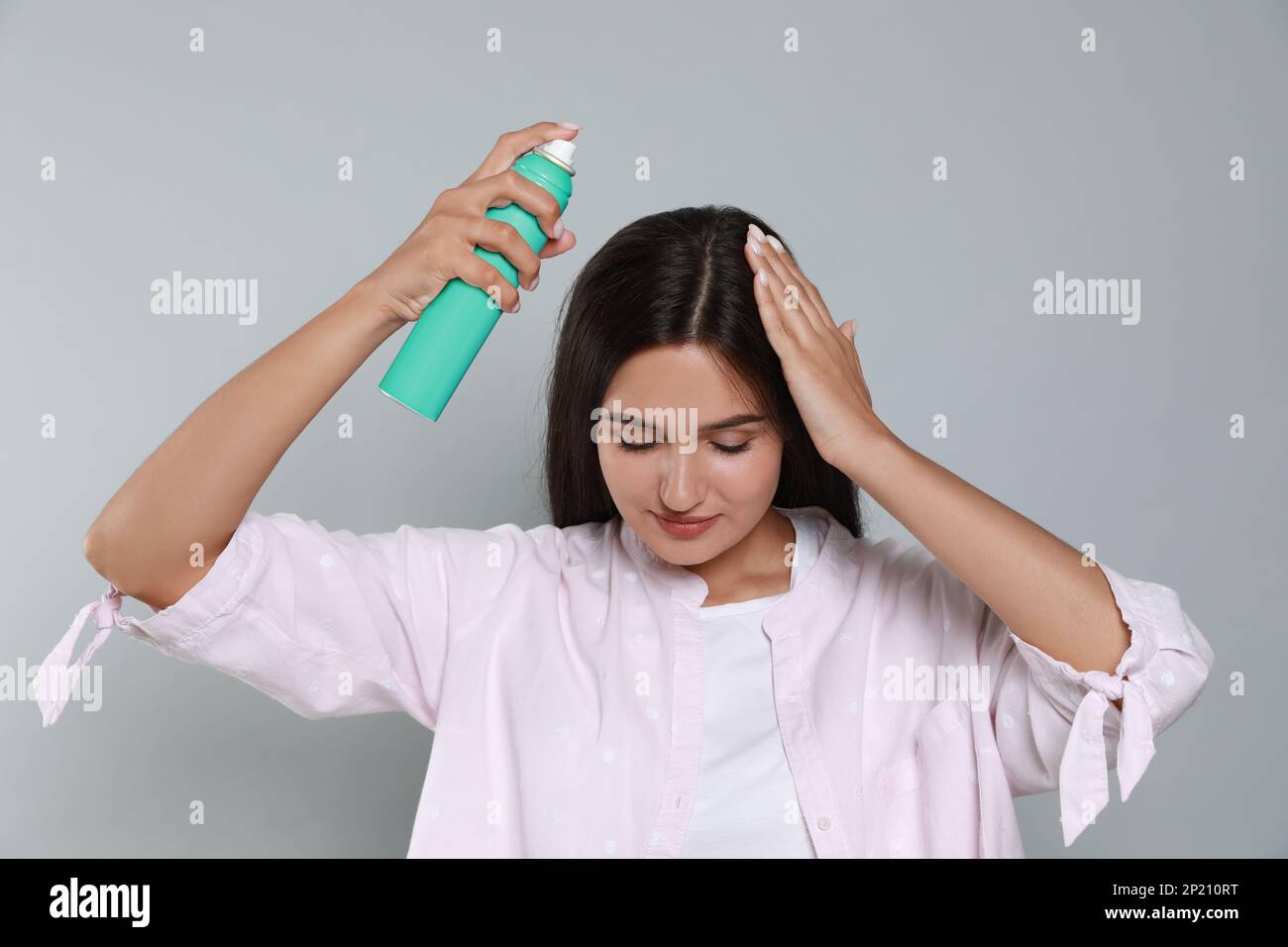 Woman applying dry shampoo onto her hair on light grey background Stock