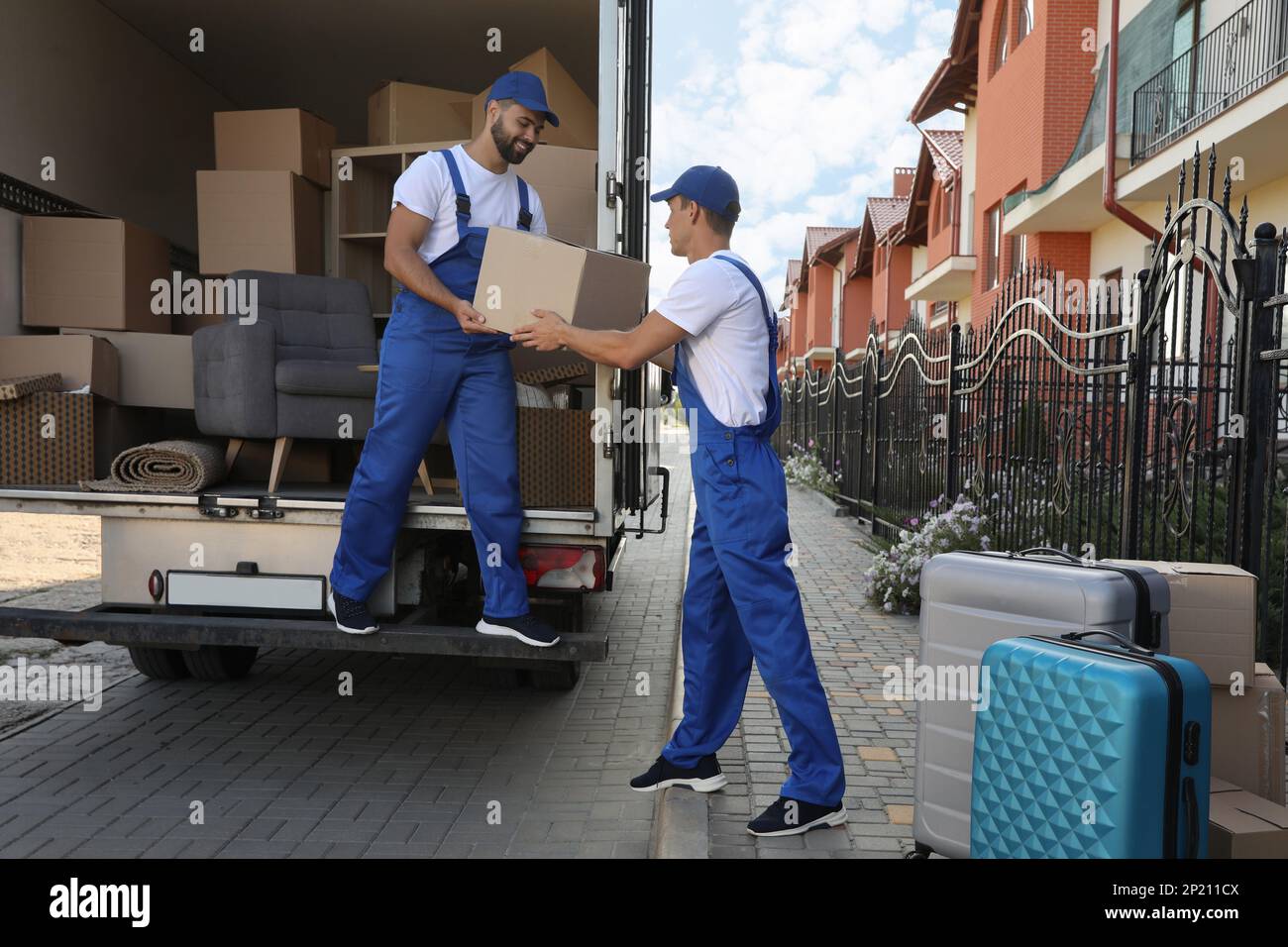 Workers unloading boxes from van outdoors. Moving service Stock Photo