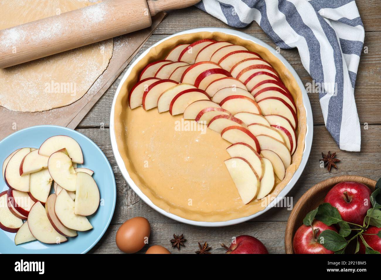 Dish with fresh apple slices and raw dough on wooden table, flat lay. Baking pie Stock Photo